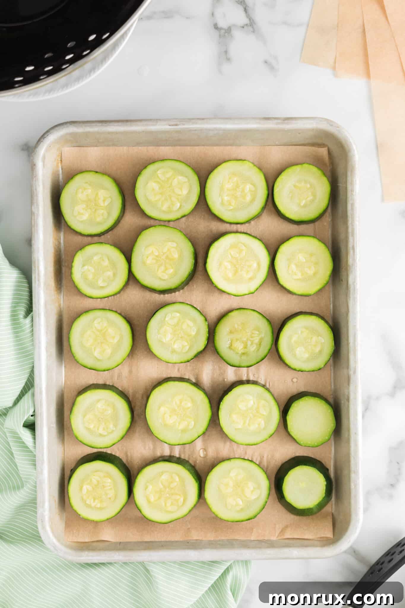 Blanched zucchini rounds meticulously arranged on a parchment-lined baking sheet, prepared for freezing.