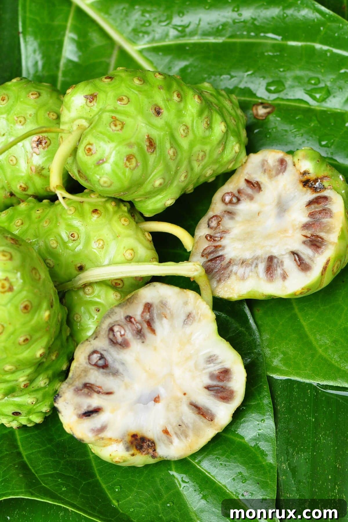 Several noni fruits, some whole and some cut in half, revealing their pale flesh and small seeds.