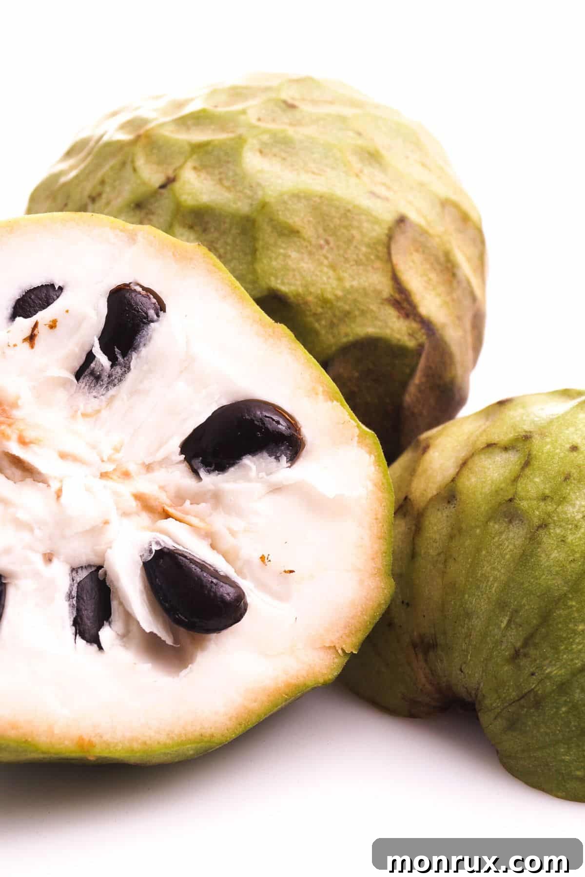 custard apple cut in half on table, revealing white flesh and black seeds.