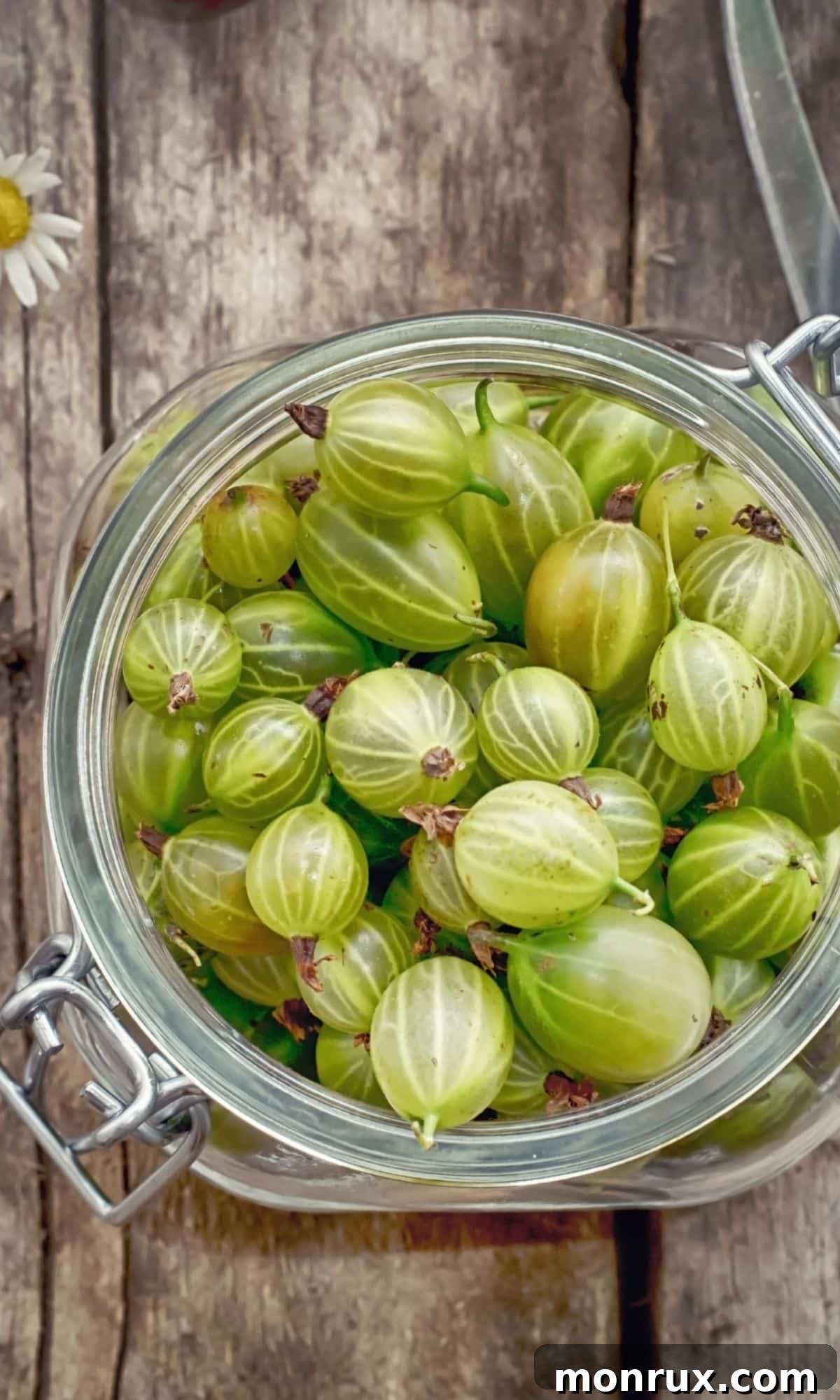 A clear jar full of tart gooseberries on a rustic wooden table.
