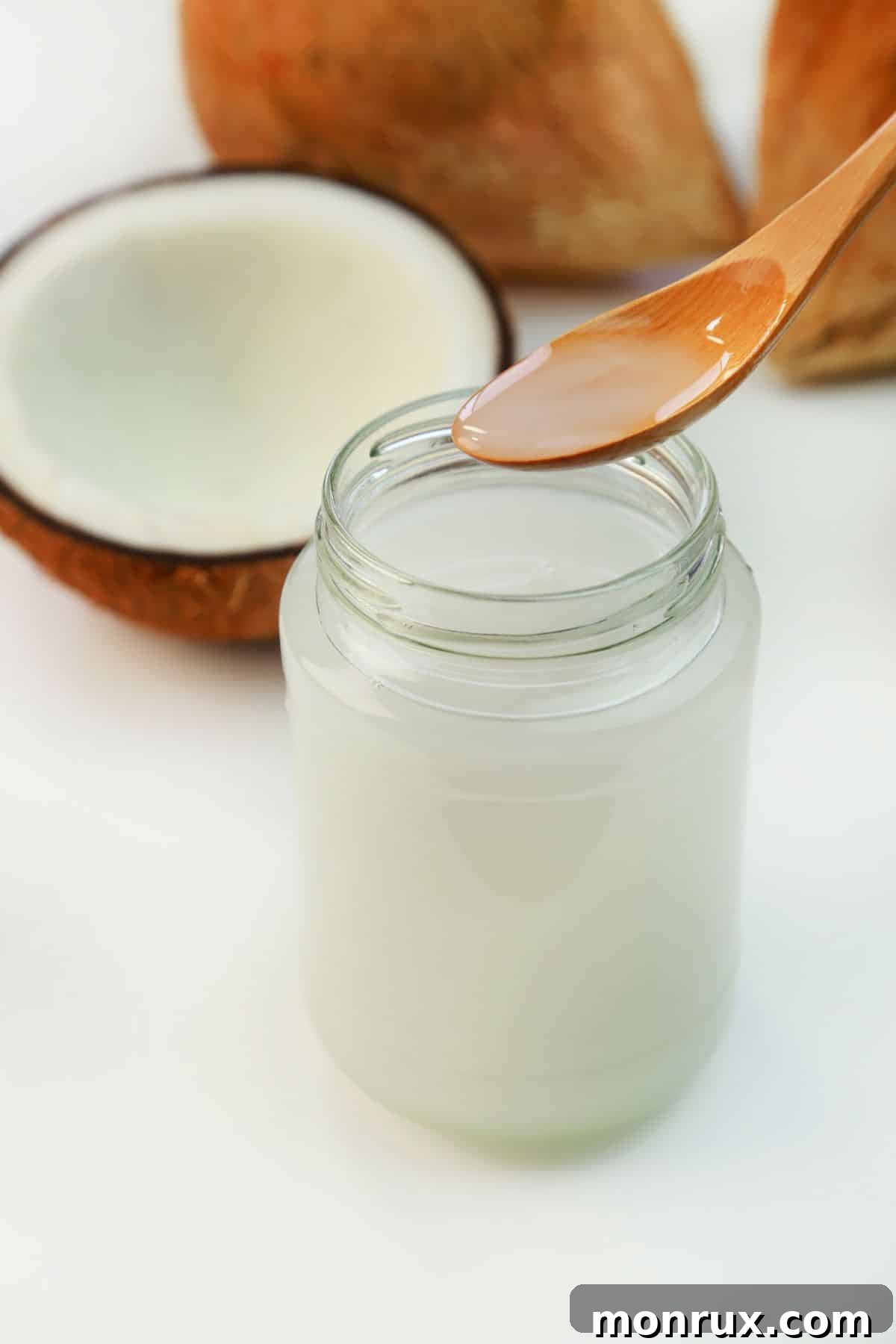 Spoon and jar of coconut oil next to a fresh coconut.
