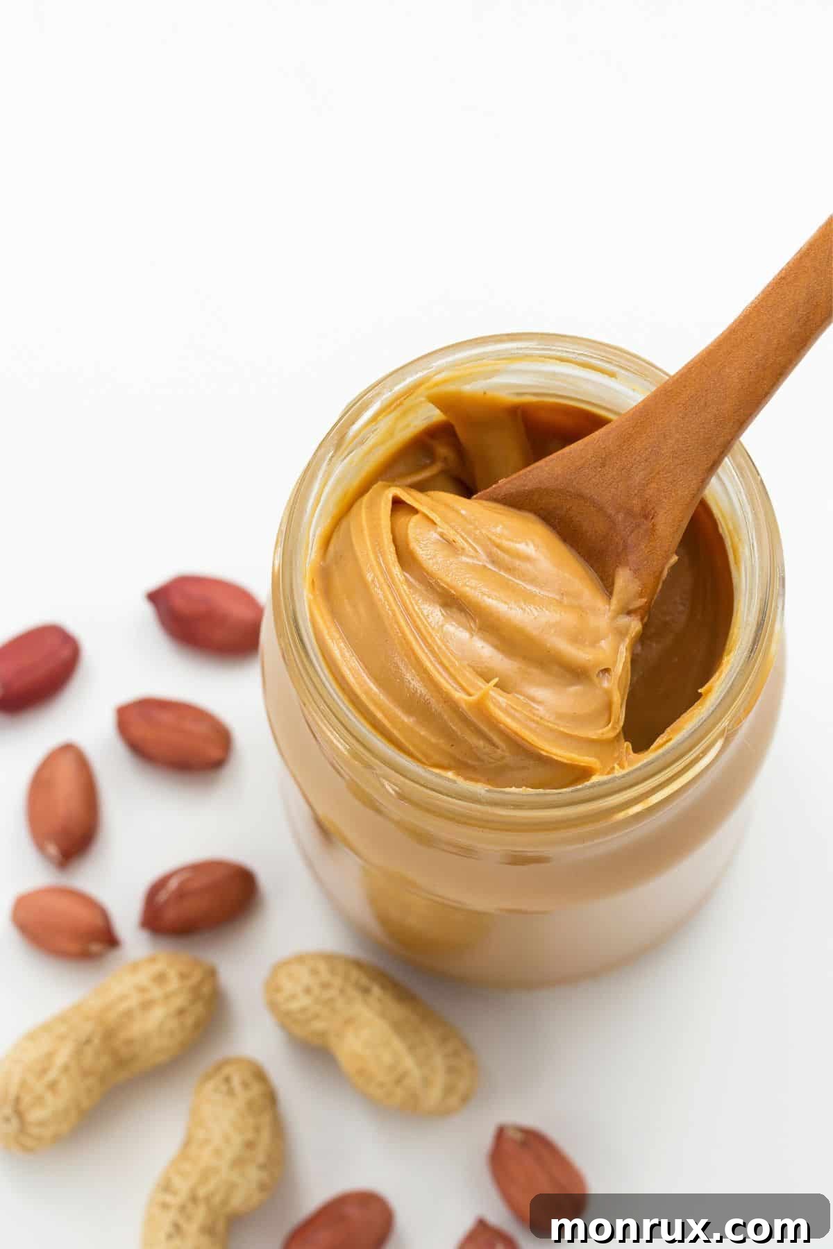 Jar of peanut butter next to scattered peanuts.