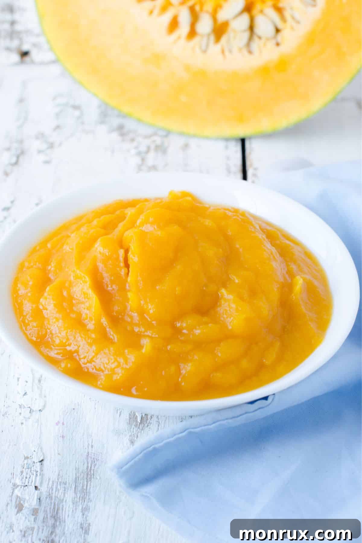Bowl of pumpkin puree beside sliced pumpkin pieces.
