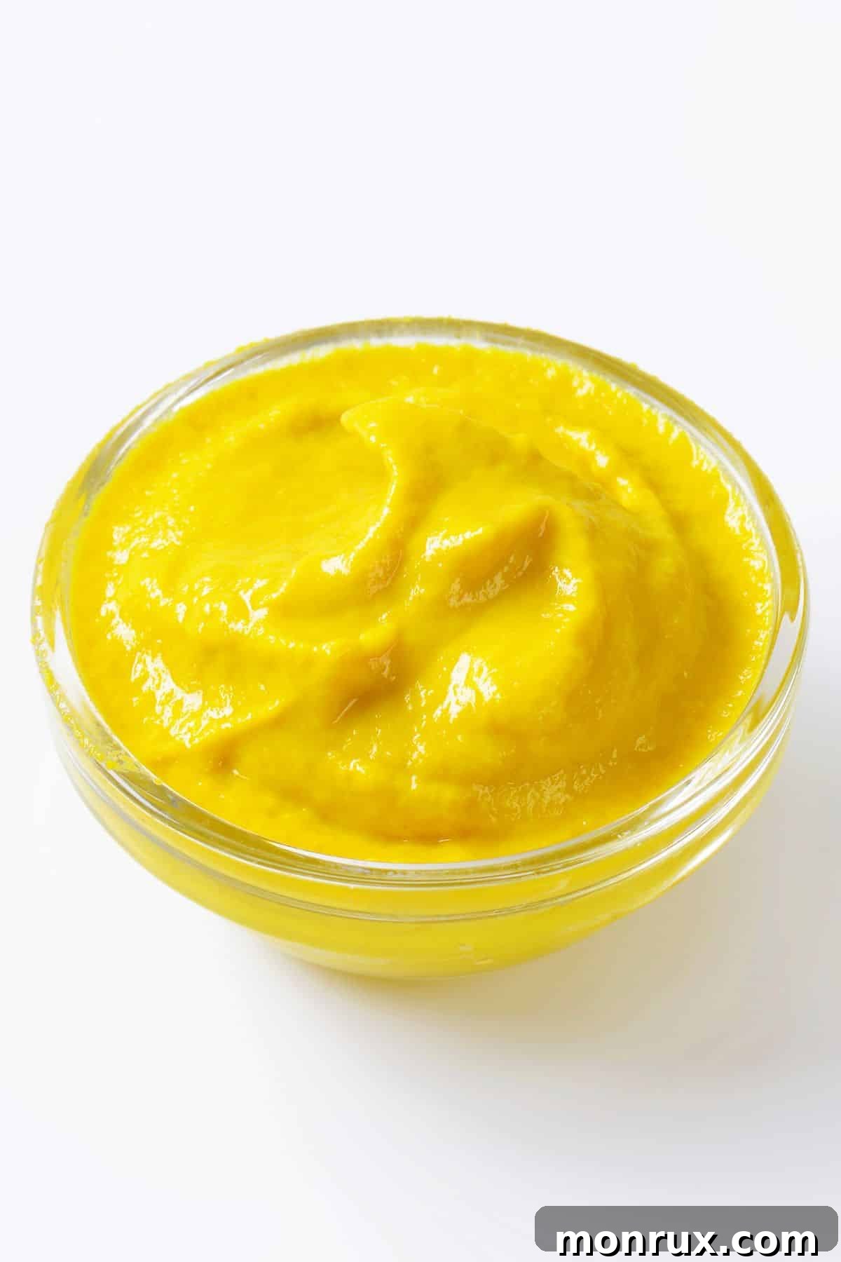 Bowl of bright yellow mustard on a clean white background.