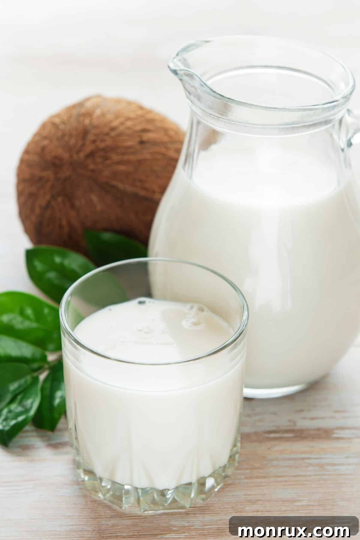 Glass of coconut milk with pitcher and whole coconut.