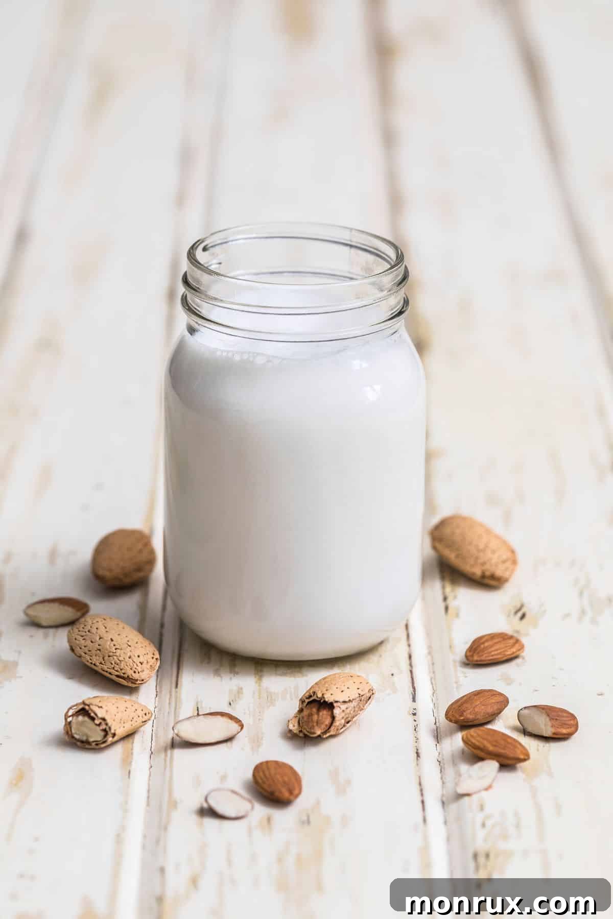Glass of almond milk with almonds on white table.