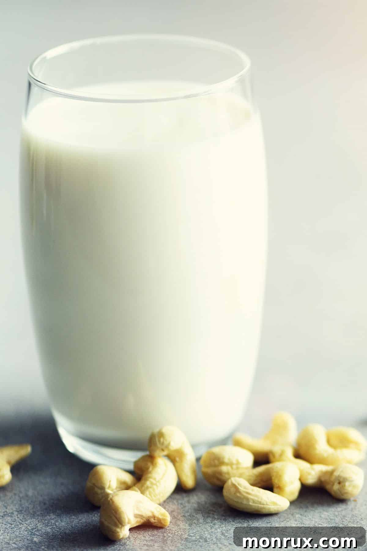 Glass of cashew milk with cashews on white table.