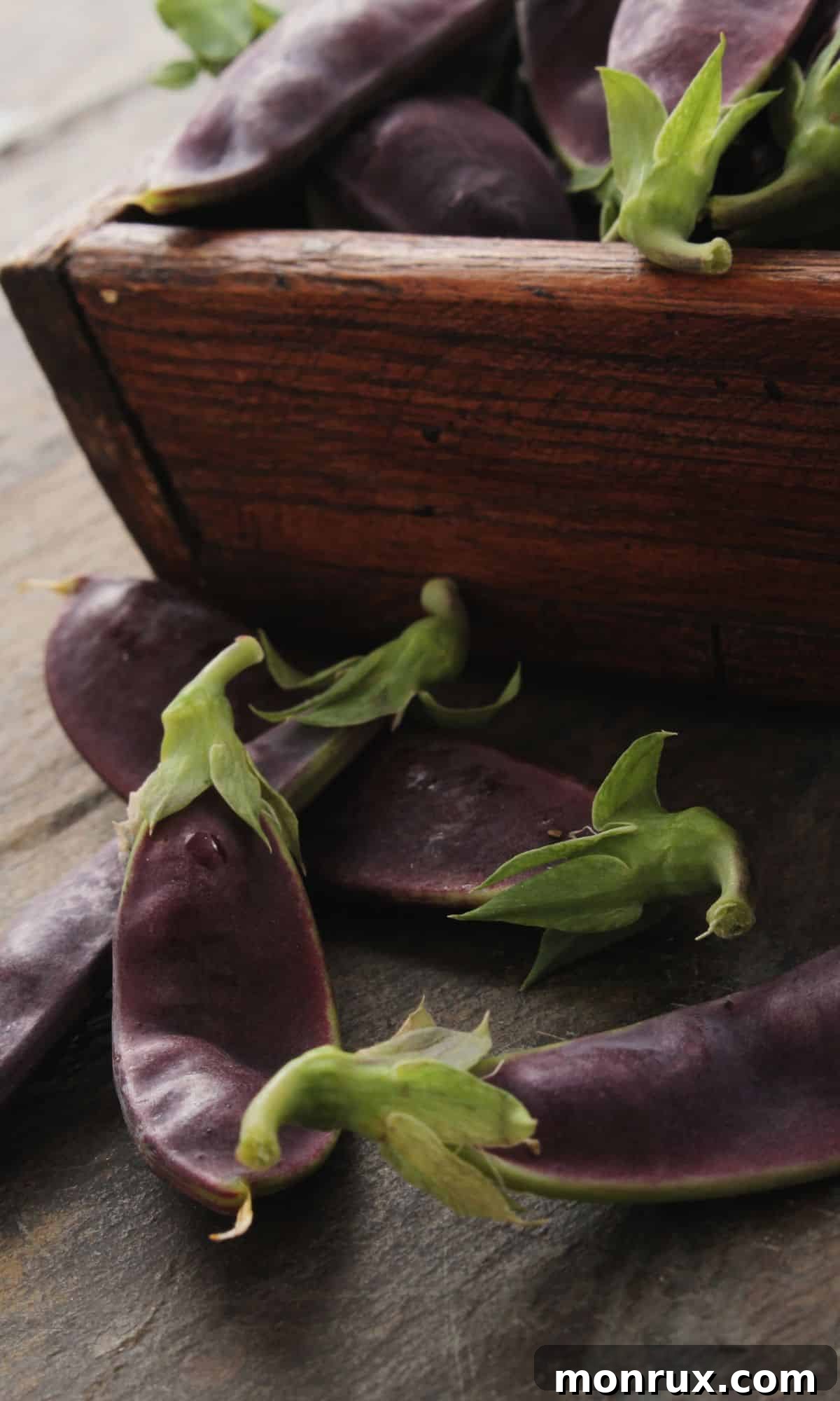 A collection of fresh Mangetout pods, also known as snow peas, resting in a rustic wooden bowl, highlighting their crisp, vibrant green appearance.
