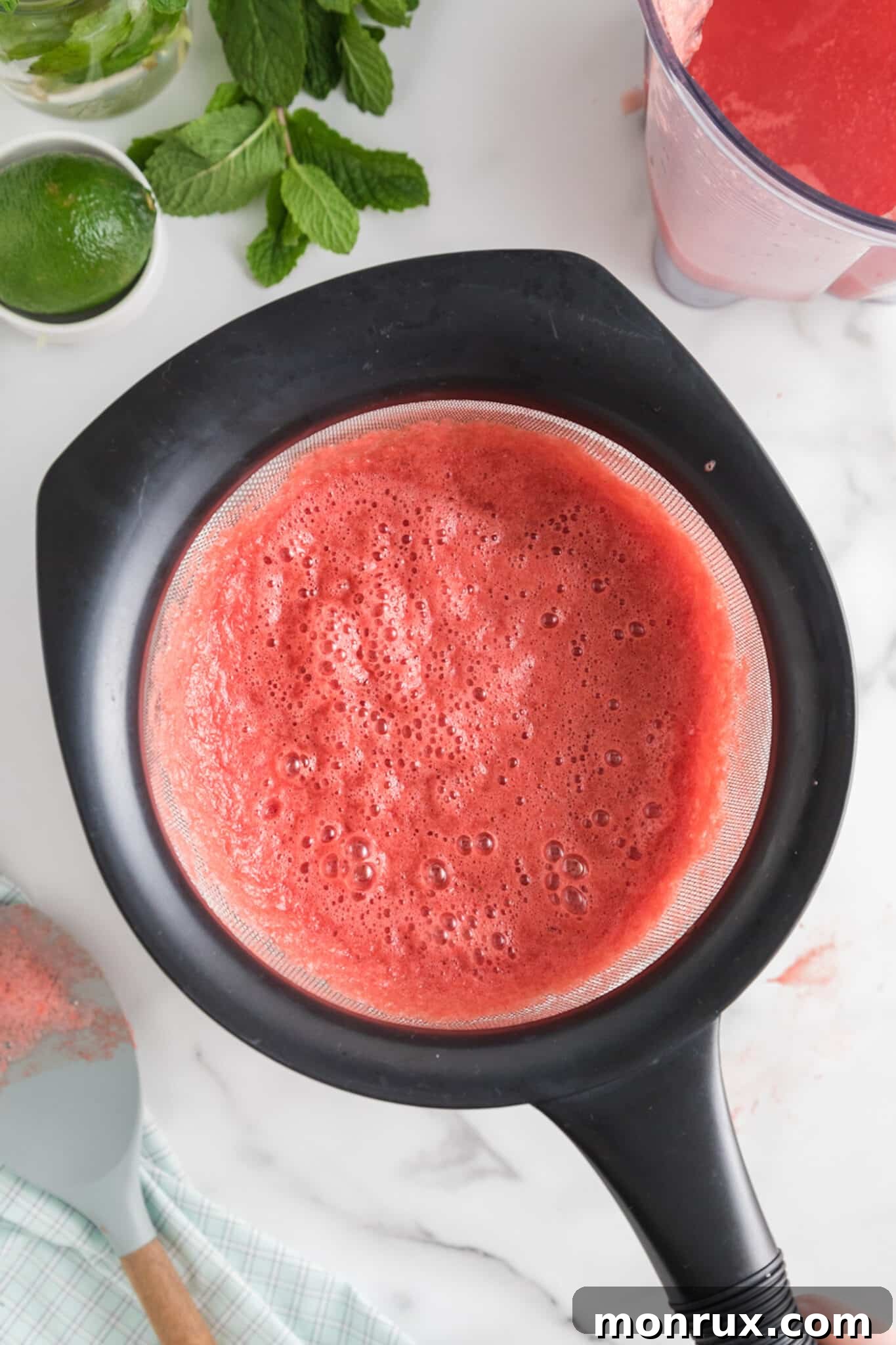 Watermelon puree being strained through a fine-mesh strainer into a bowl, demonstrating a step in the cocktail preparation.