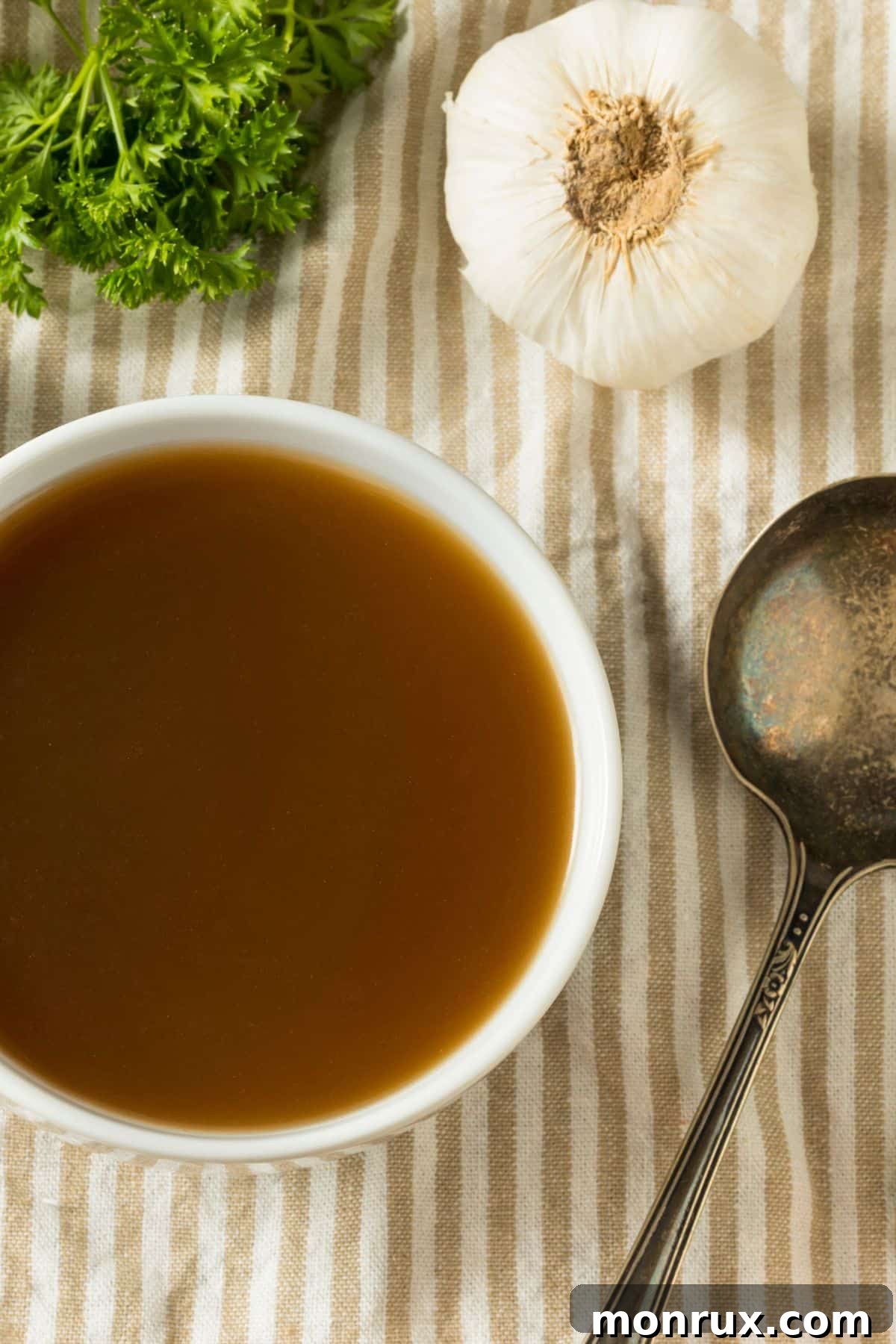 Bowl of rich beef broth with fresh vegetables on a rustic wooden table.