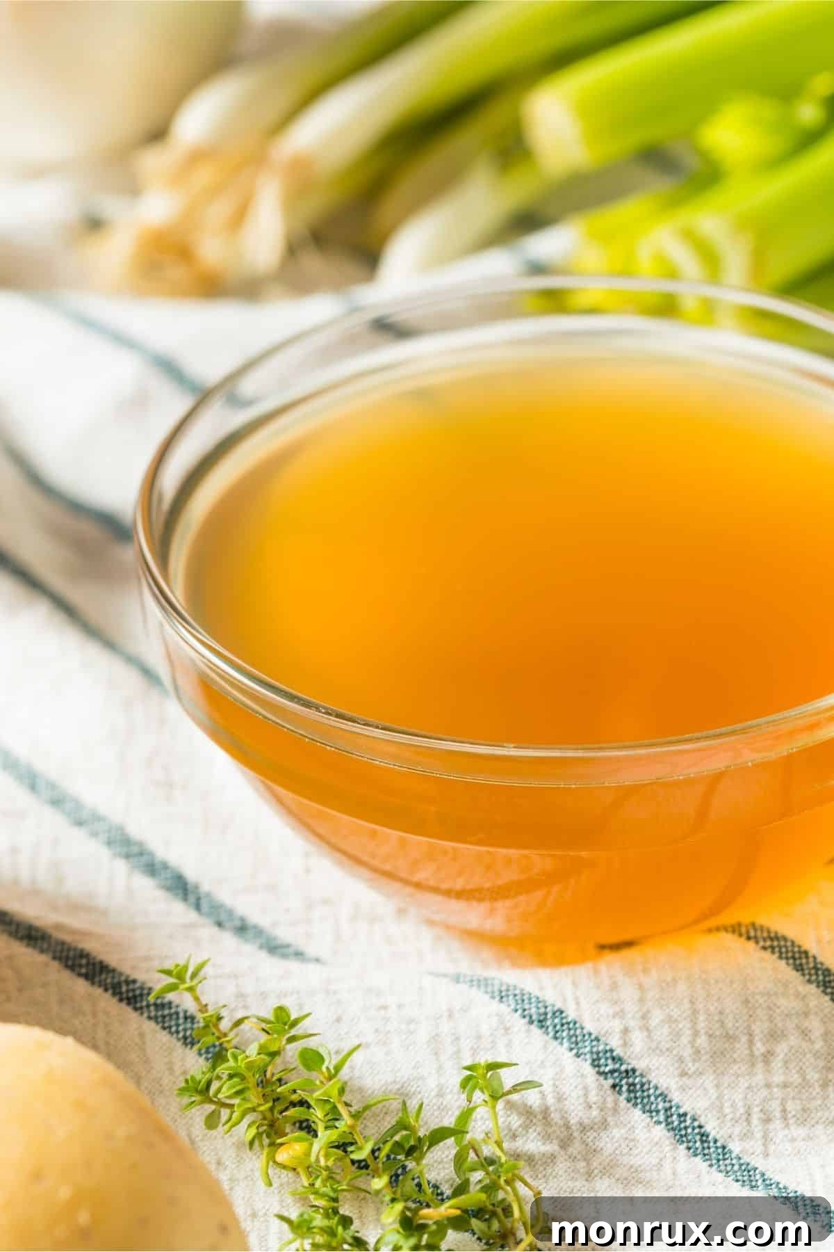 Bowl of golden vegetable broth with assorted fresh vegetables and herbs.