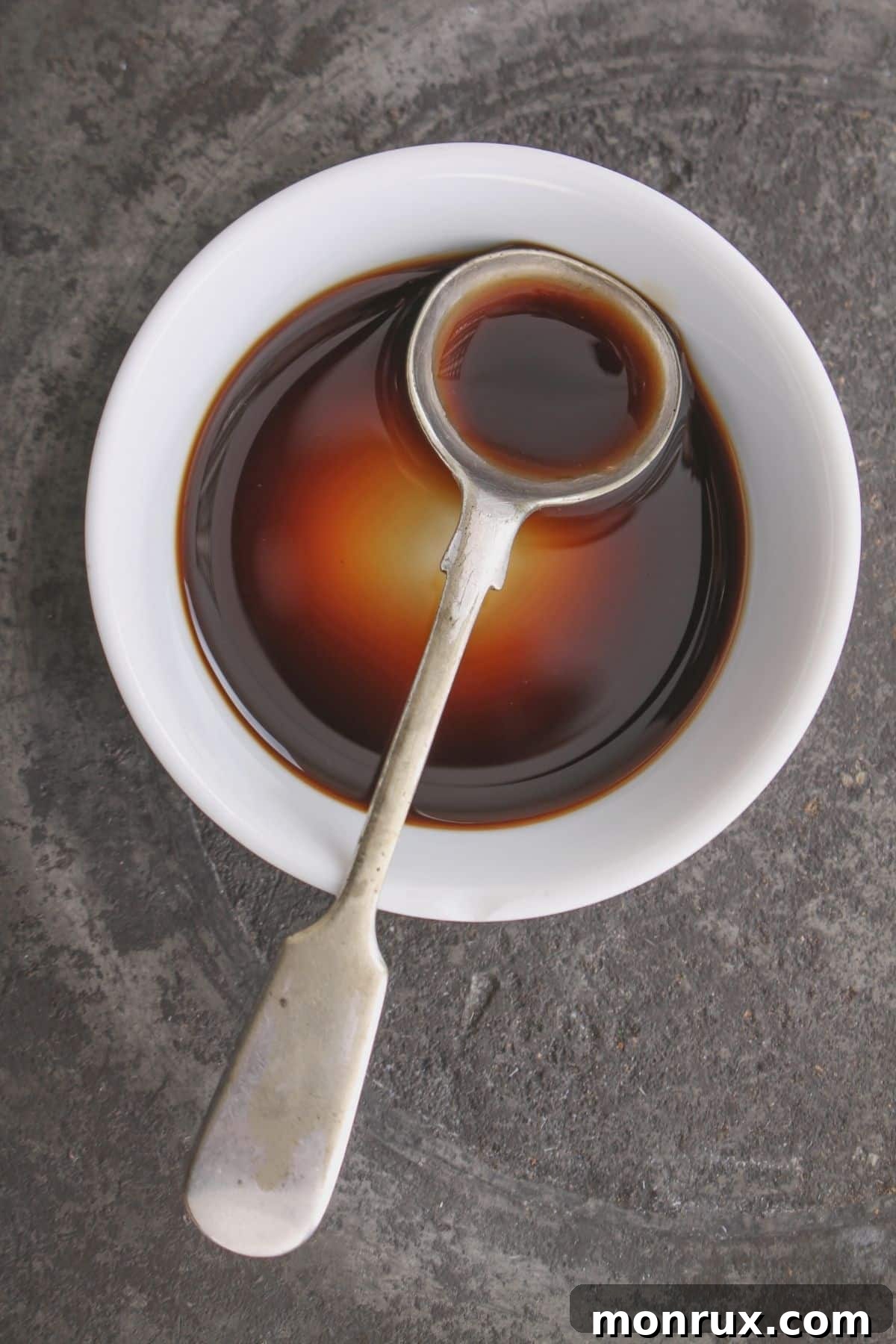A small bowl of liquid aminos with a spoon, highlighting its dark, savory liquid.