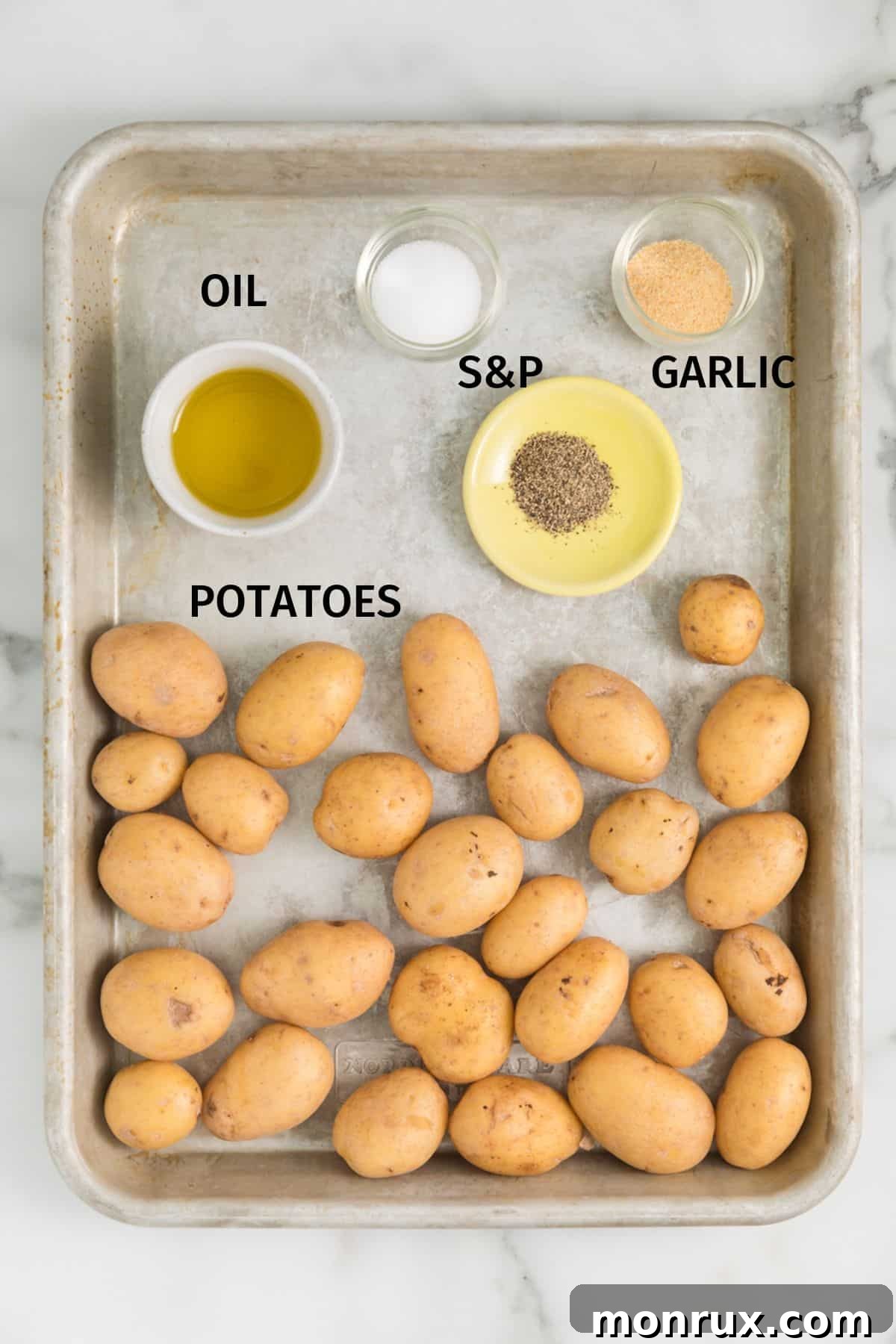 A baking sheet showcasing the simple, fresh ingredients required to make air fryer smashed potatoes: small potatoes, olive oil, salt, pepper, and garlic powder.