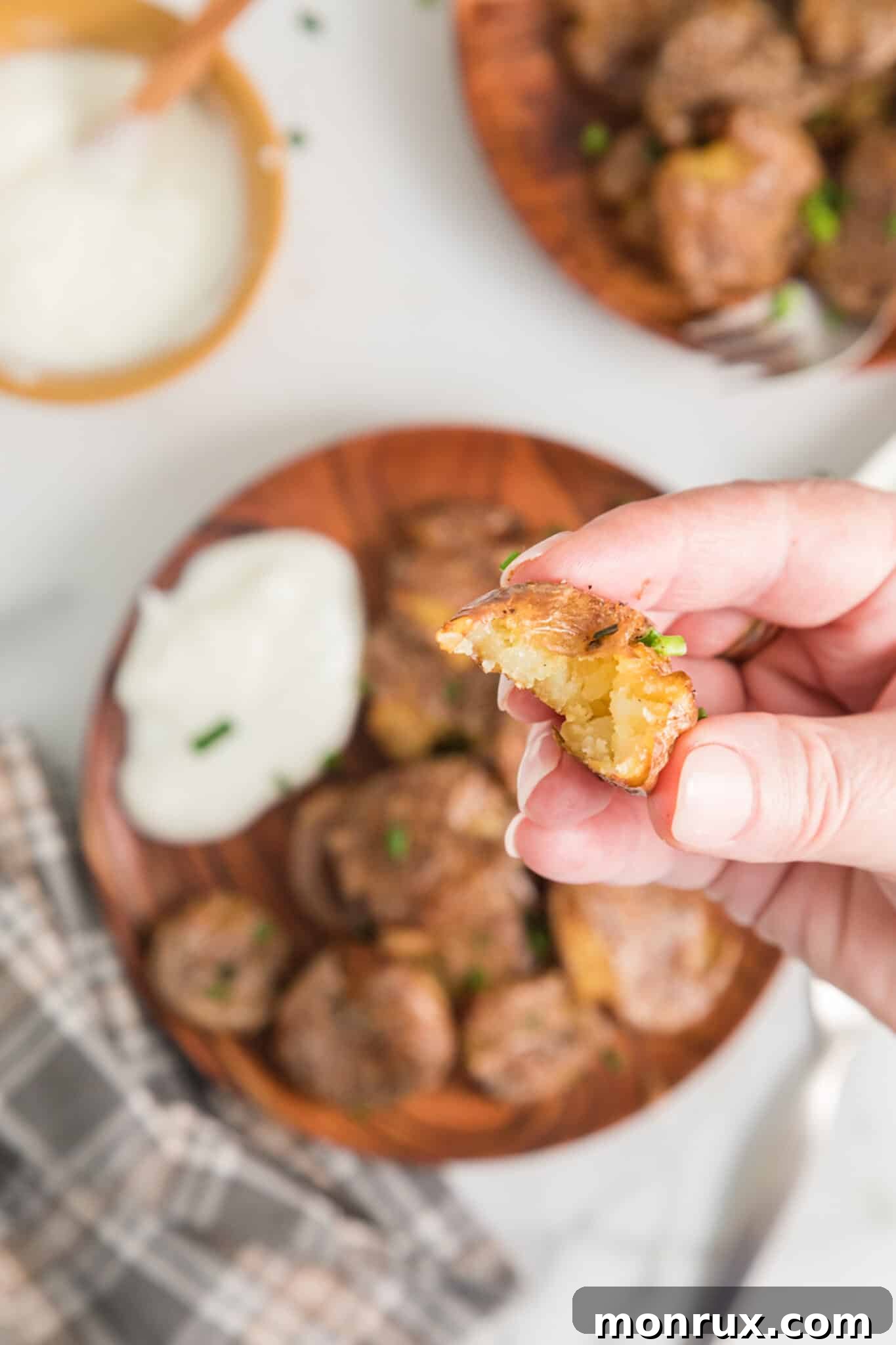 A hand holding a perfectly cooked air fryer smashed potato, with a bite taken out, revealing its fluffy interior.