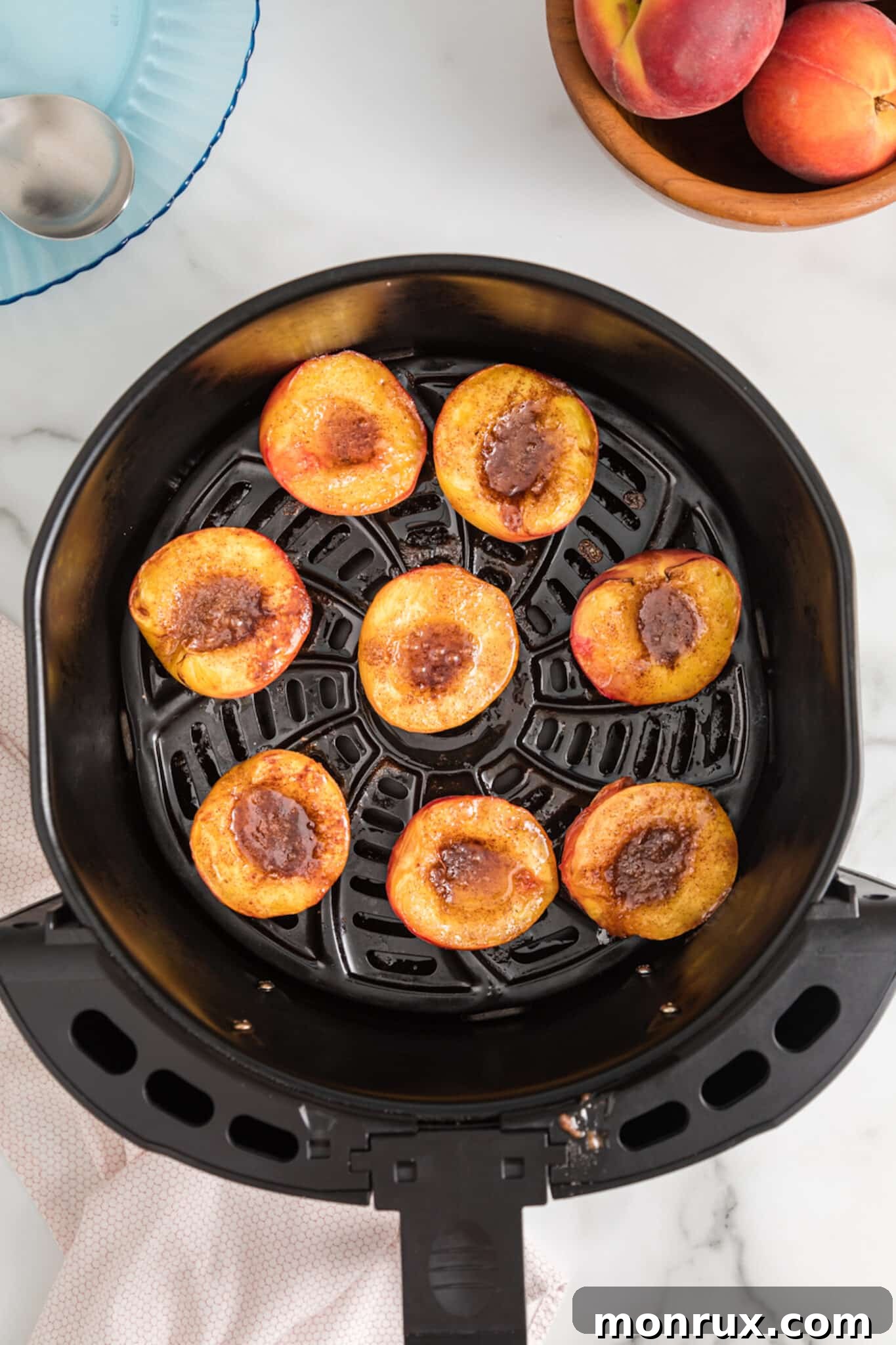 The fourth step for air fried peaches, showing the cooked peach halves flipped cut-side up in the air fryer basket, with a spoonful of the butter, sugar, and cinnamon topping being carefully placed into the hollow of each peach.