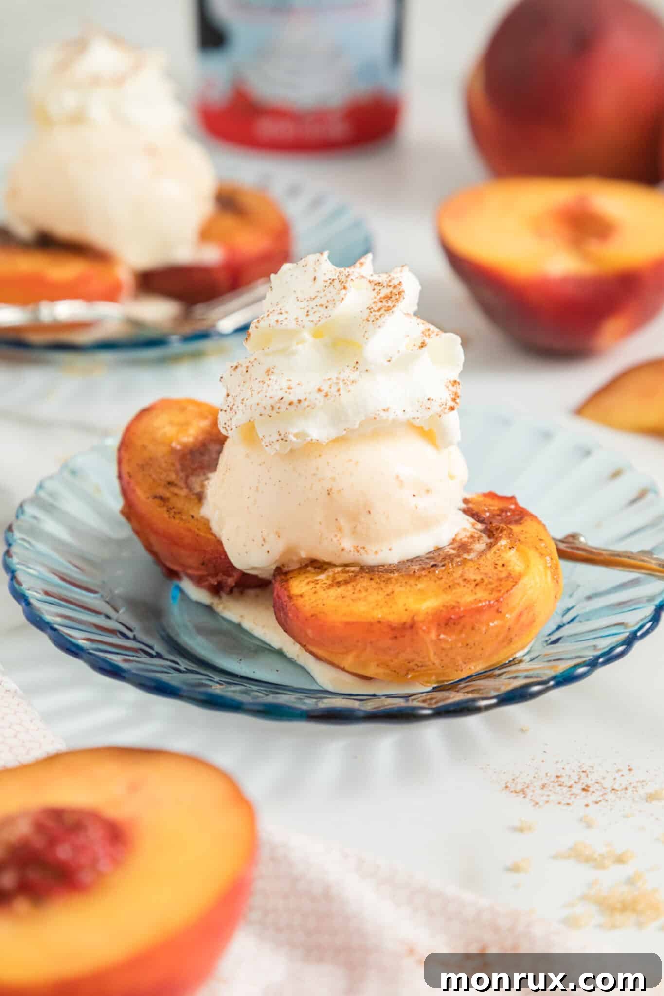 Two perfectly air fried peach halves served on a white dessert plate, generously topped with a scoop of creamy vanilla ice cream, creating an irresistible summer dessert.