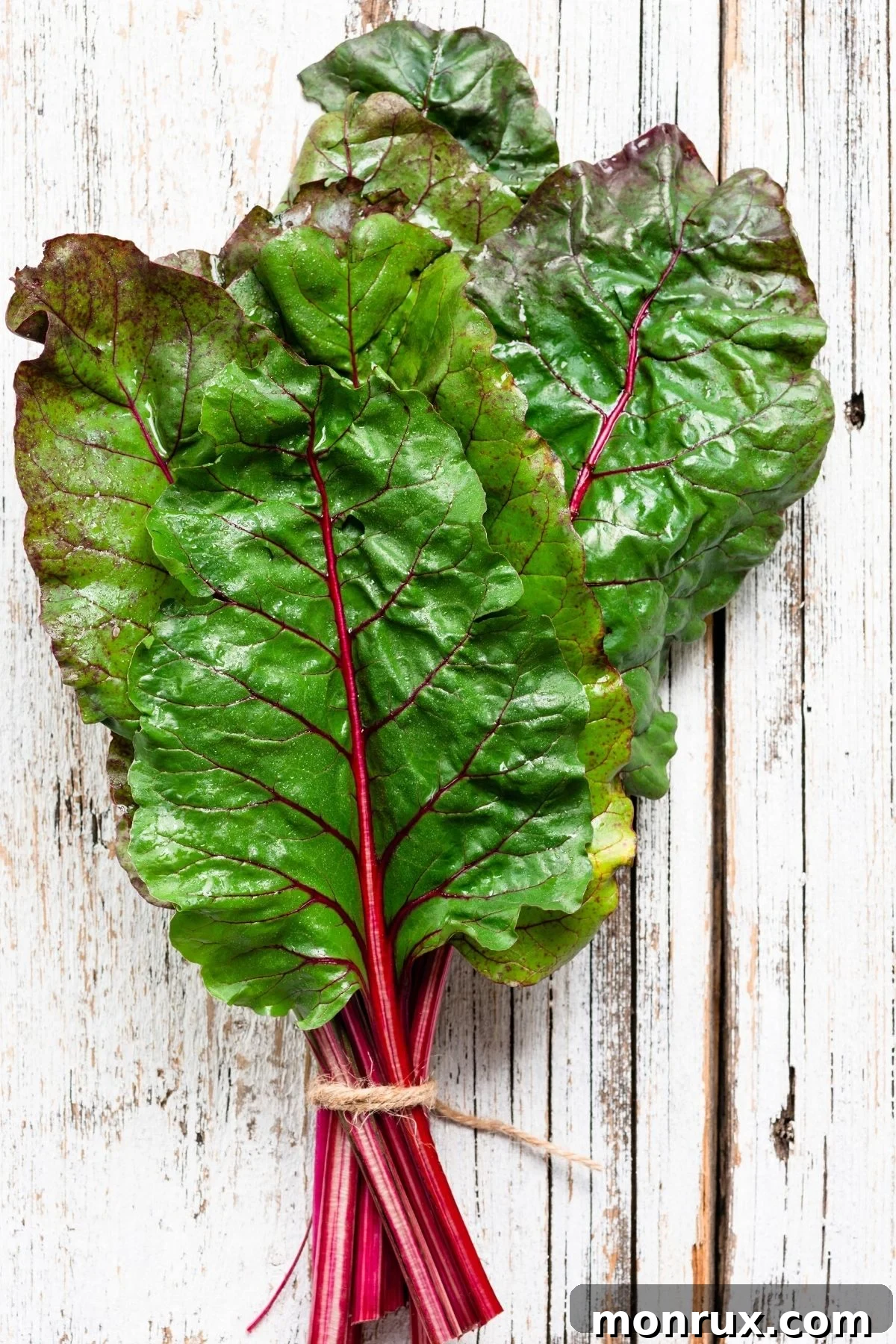 Vibrant Swiss chard with colorful stalks and dark green leaves on a wooden table, emphasizing its visual appeal.