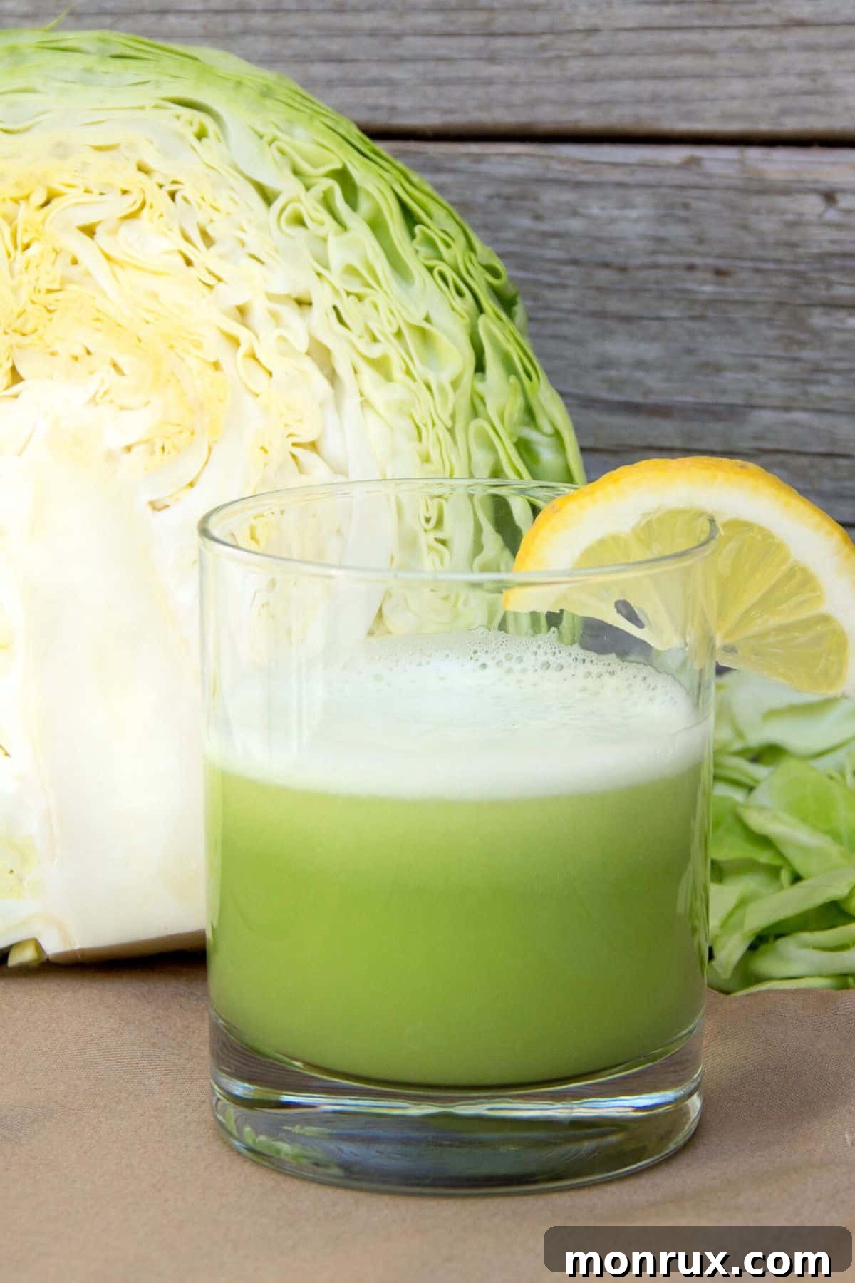A glass of freshly made cabbage juice sits in front of a halved head of green cabbage, highlighting its health potential.