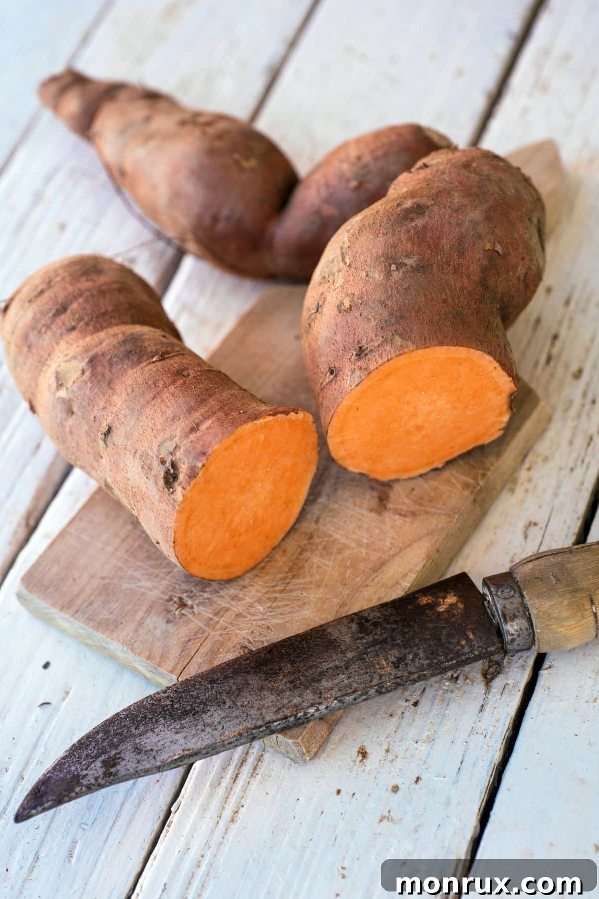 A vibrant orange sweet potato, halved to show its rich color and smooth texture, on a cutting board.