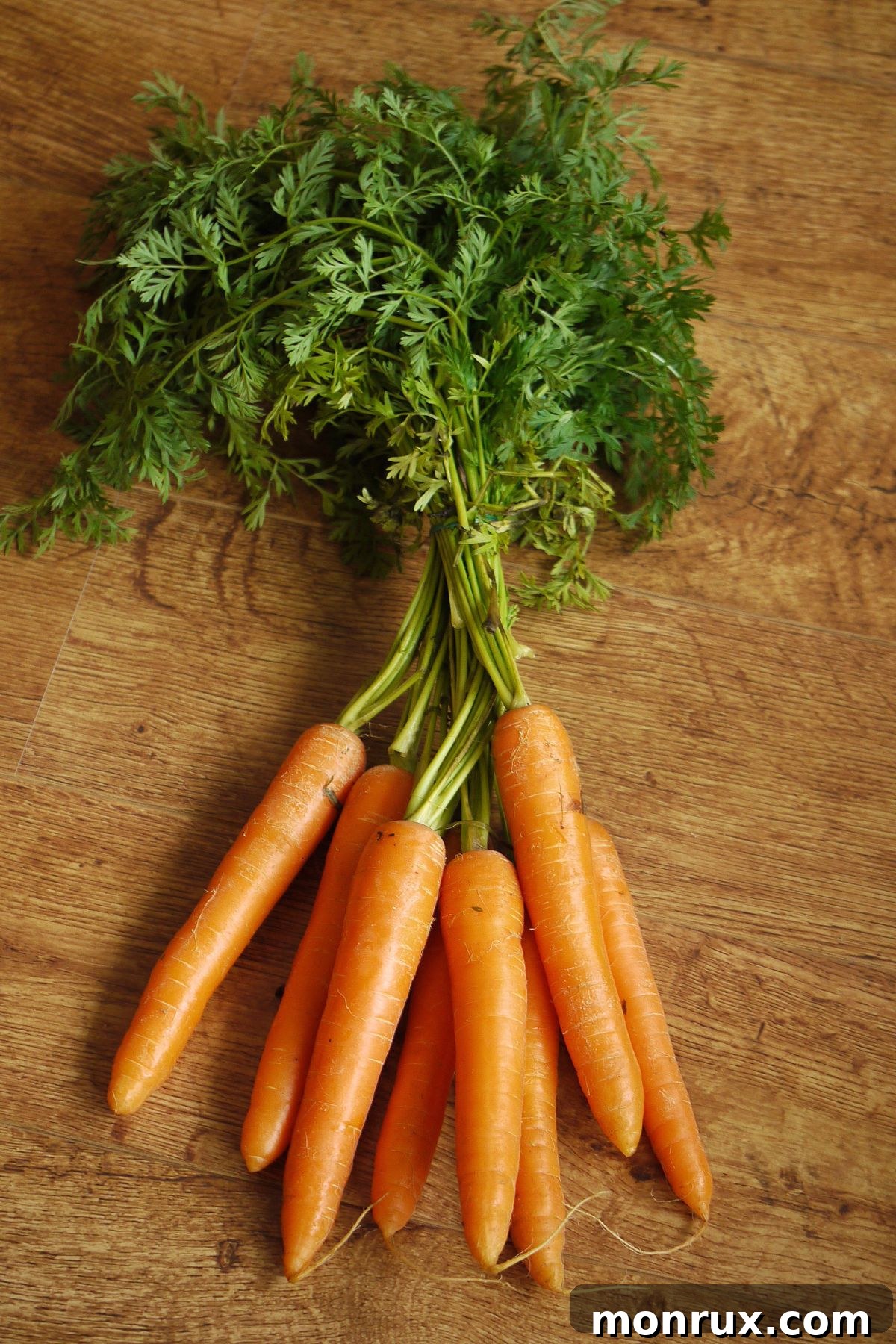 A vibrant bunch of small carrots with their green tops on a wooden table, ready for juicing.
