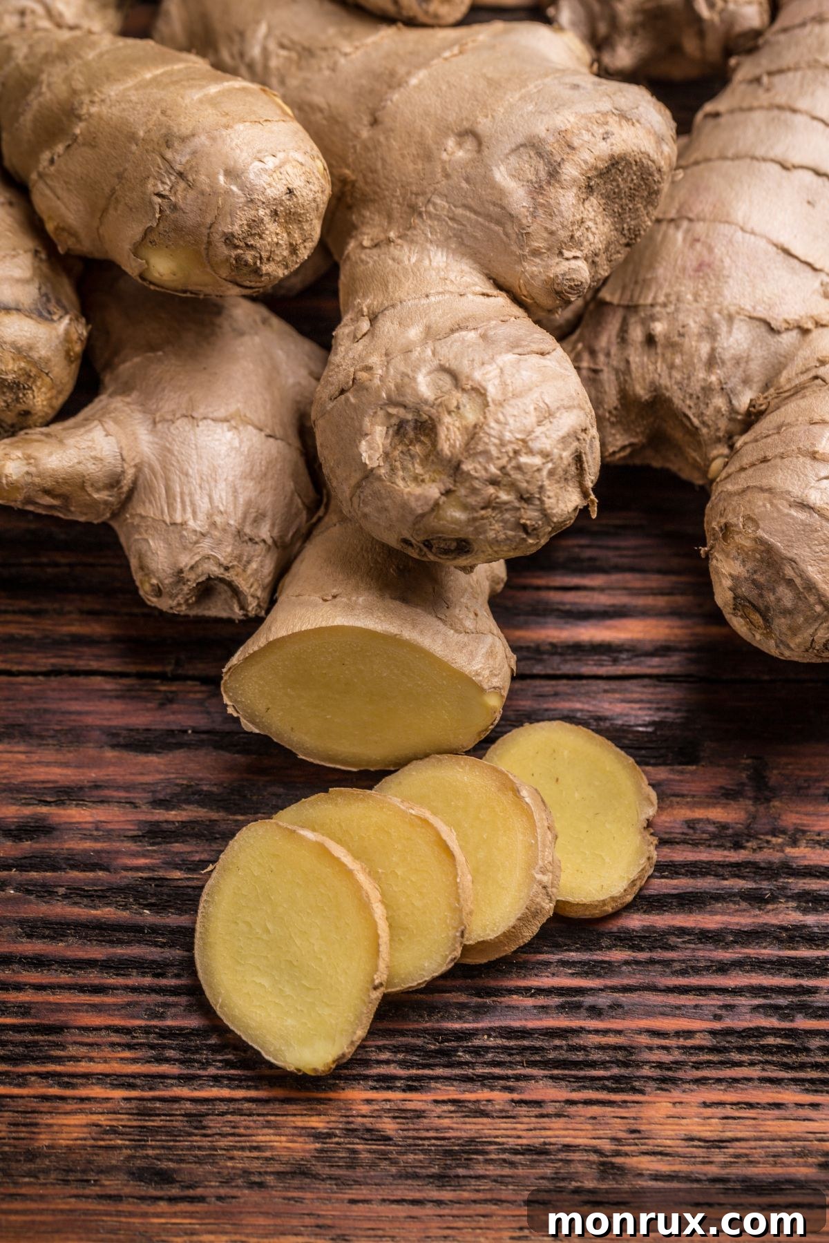 Rough fingers of fresh ginger root and thinly sliced pieces on a rustic wooden surface, ready for culinary use.