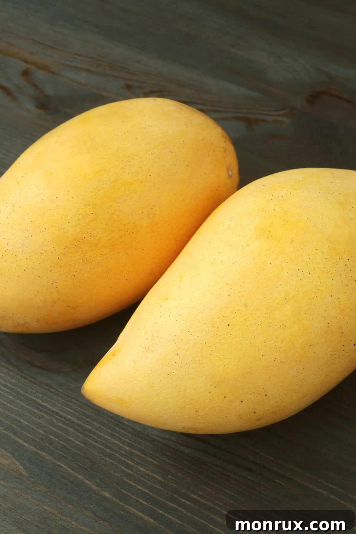 Several ripe, golden-yellow Nam Dok Mai mangoes on a dark wooden surface.
