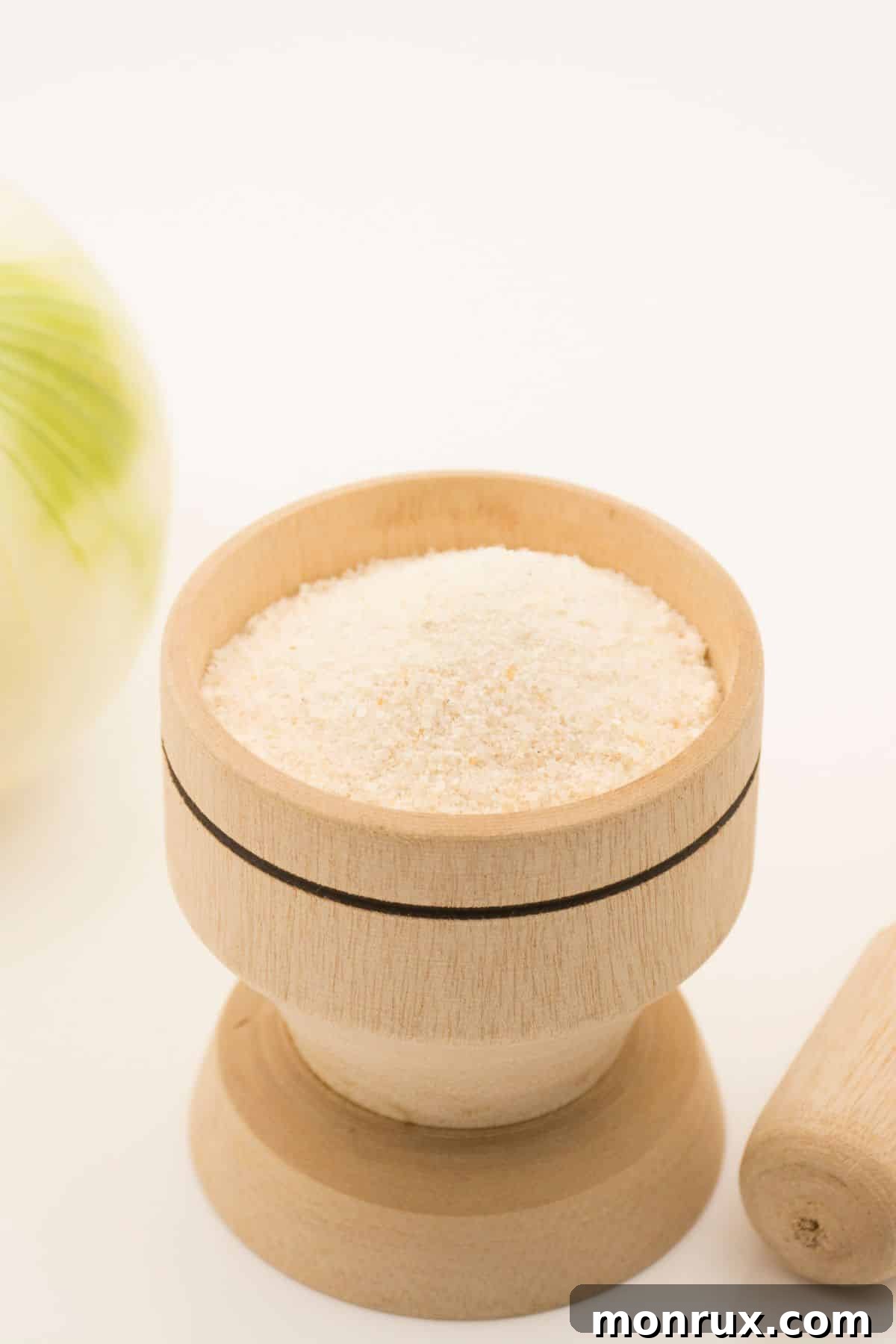 A container of onion powder sitting next to a fresh white onion, illustrating the versatility of onion in both powdered and whole forms.