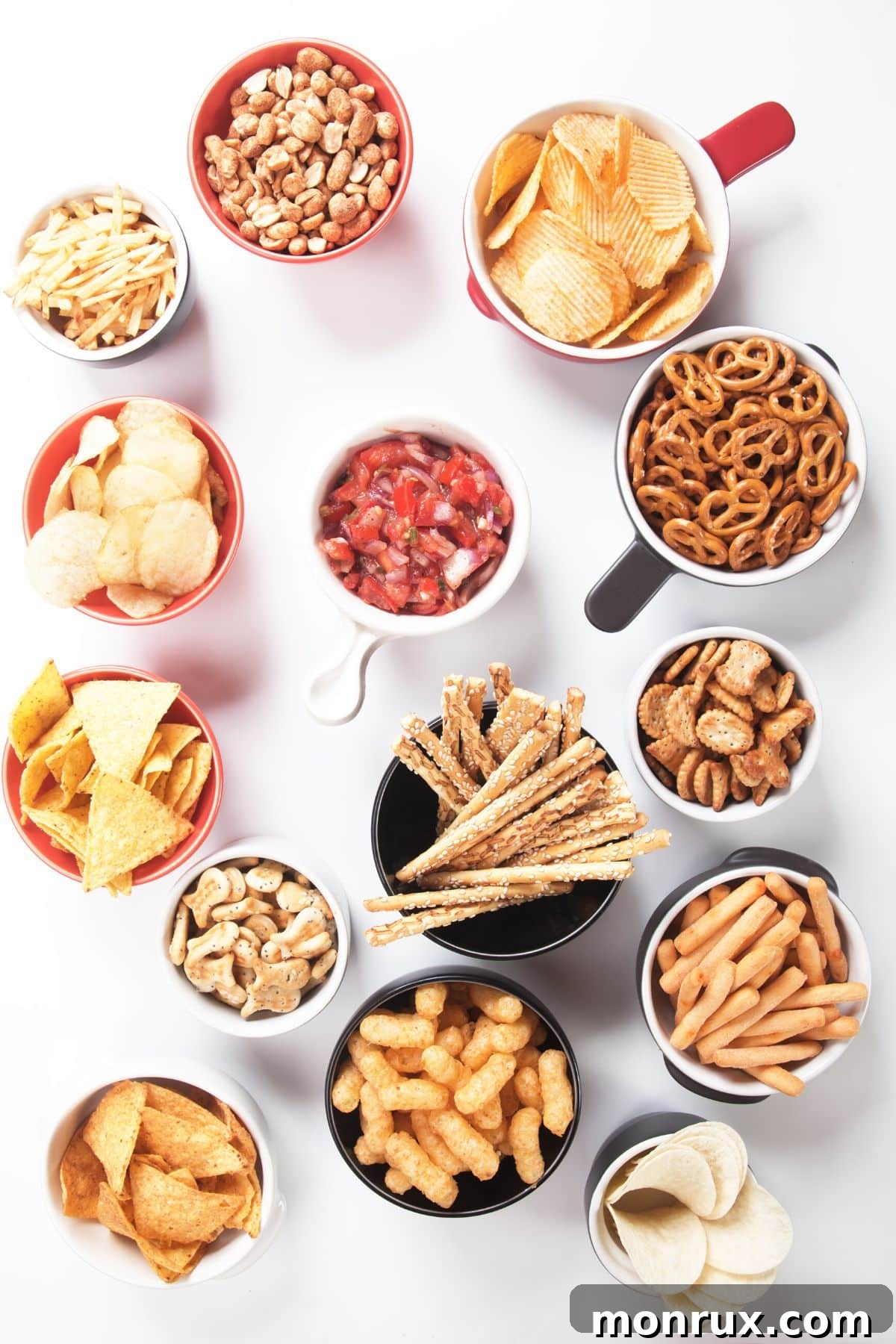 Various healthy snacks arranged in small cups and bowls on a clean white surface, showcasing an array of colors and textures.