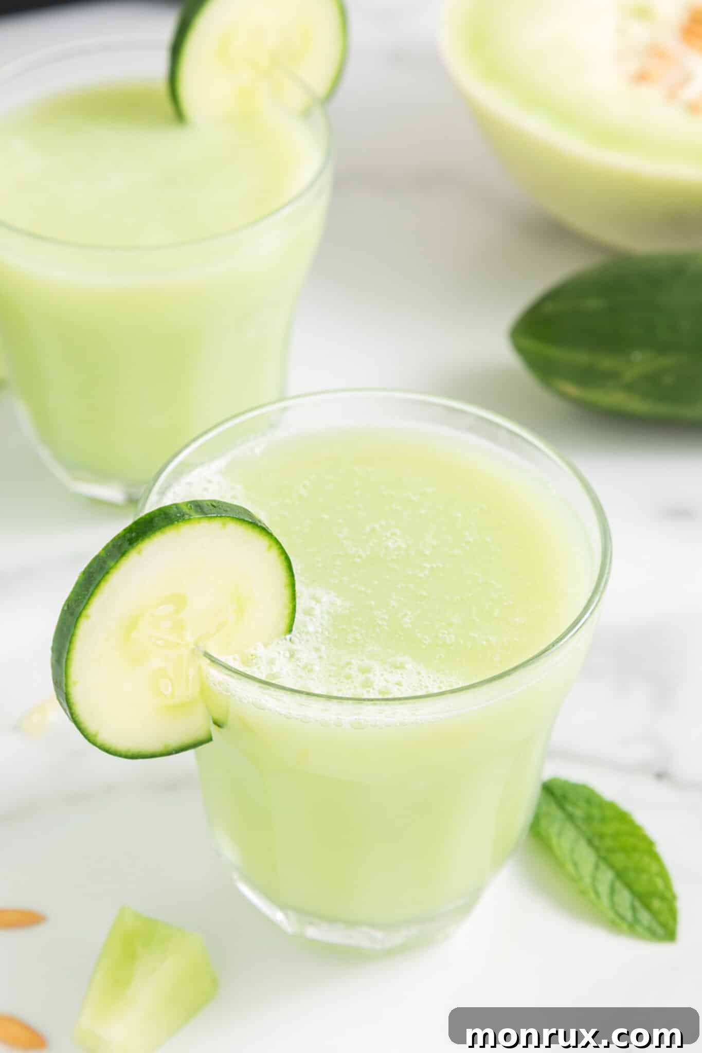 Two glasses of vibrant honeydew cucumber smoothie garnished with fresh mint, sitting on a kitchen countertop.