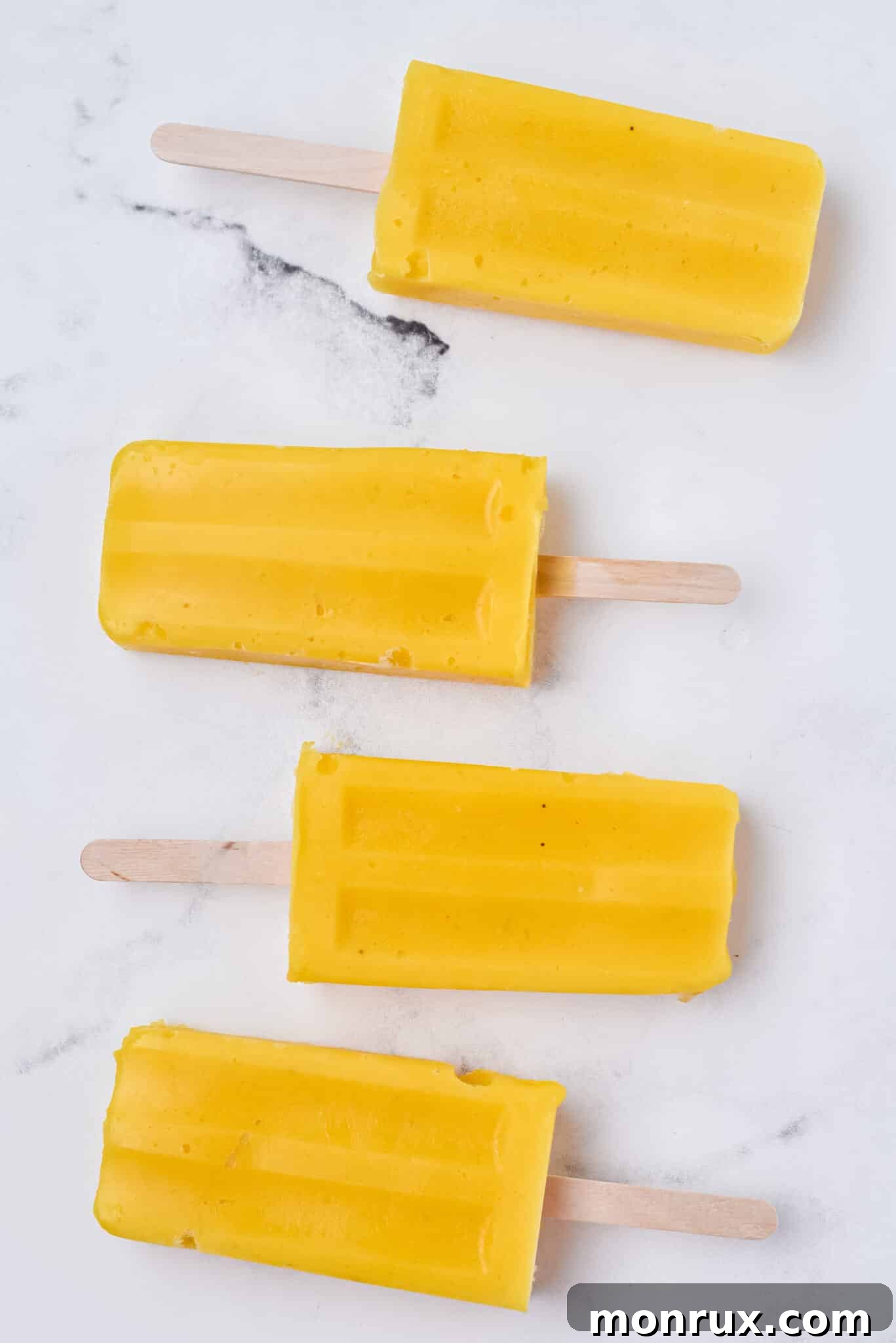 Four vibrant homemade mango popsicles neatly arranged on a sleek marble table, showcasing their refreshing appeal and bright natural color.