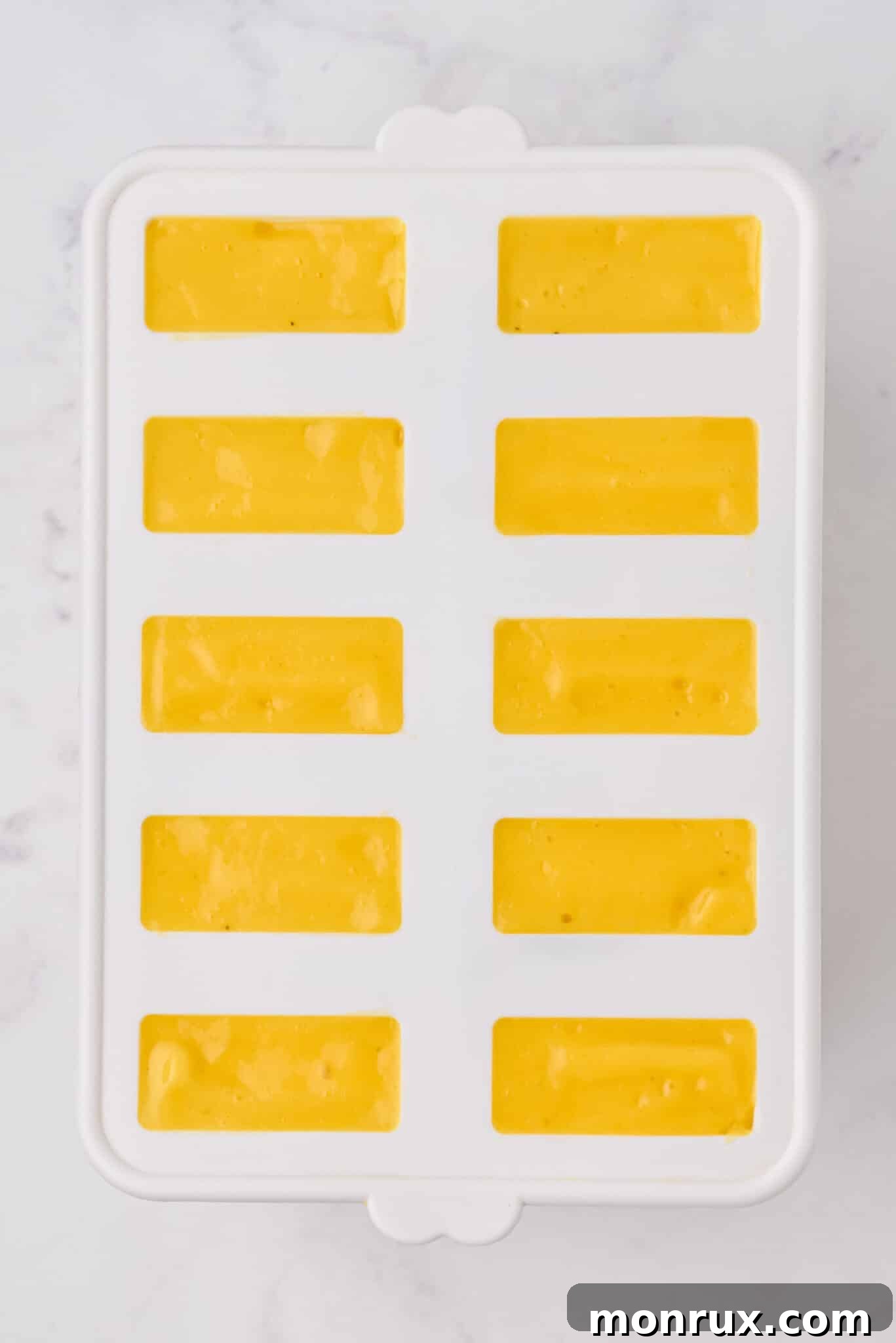 Smooth and creamy mango popsicle mixture poured into silicone molds, perfectly prepared and ready for freezing.