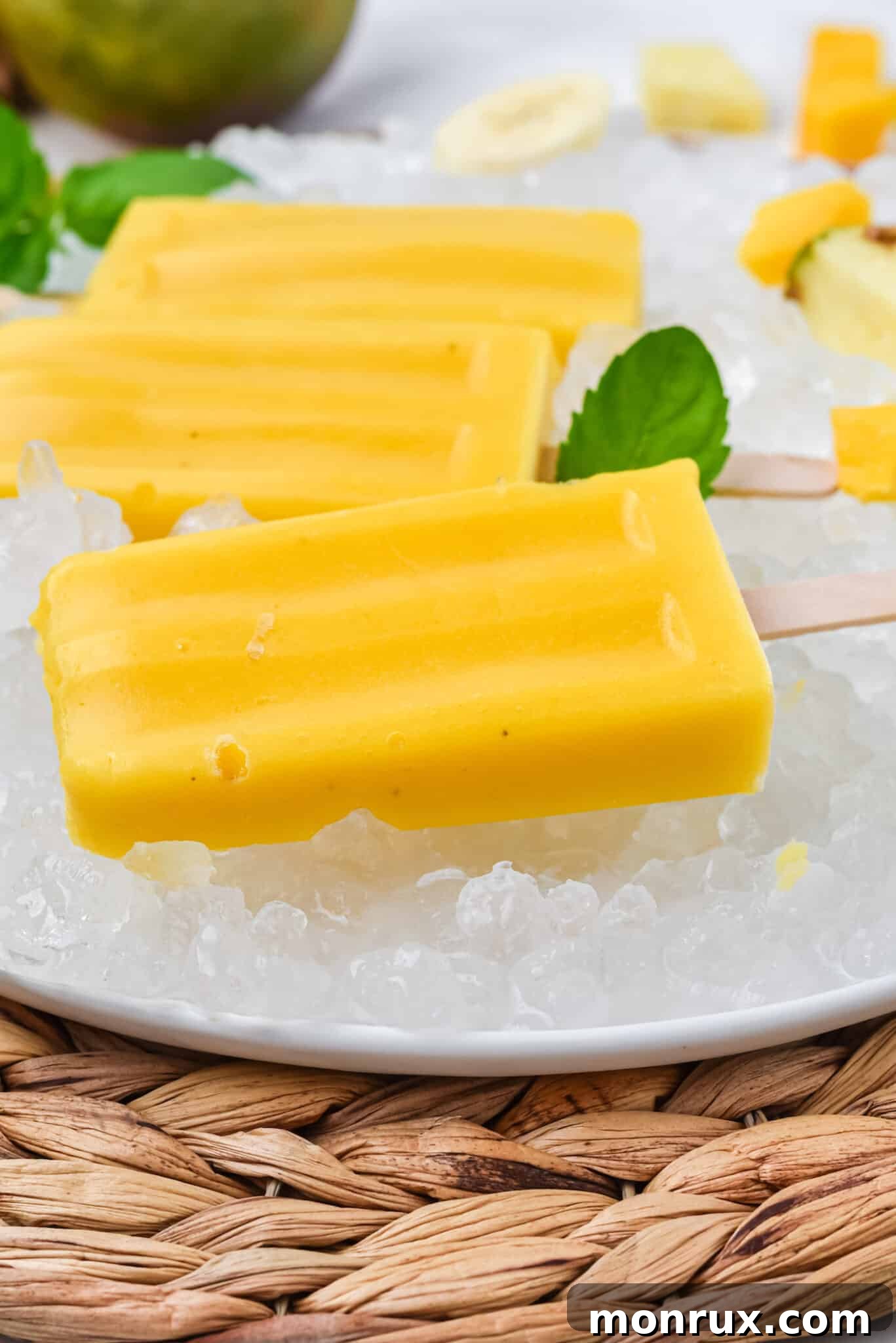 Three perfectly frozen mango popsicles presented on a sleek plate, kept cool with surrounding ice, ready to be enjoyed as a refreshing dessert.