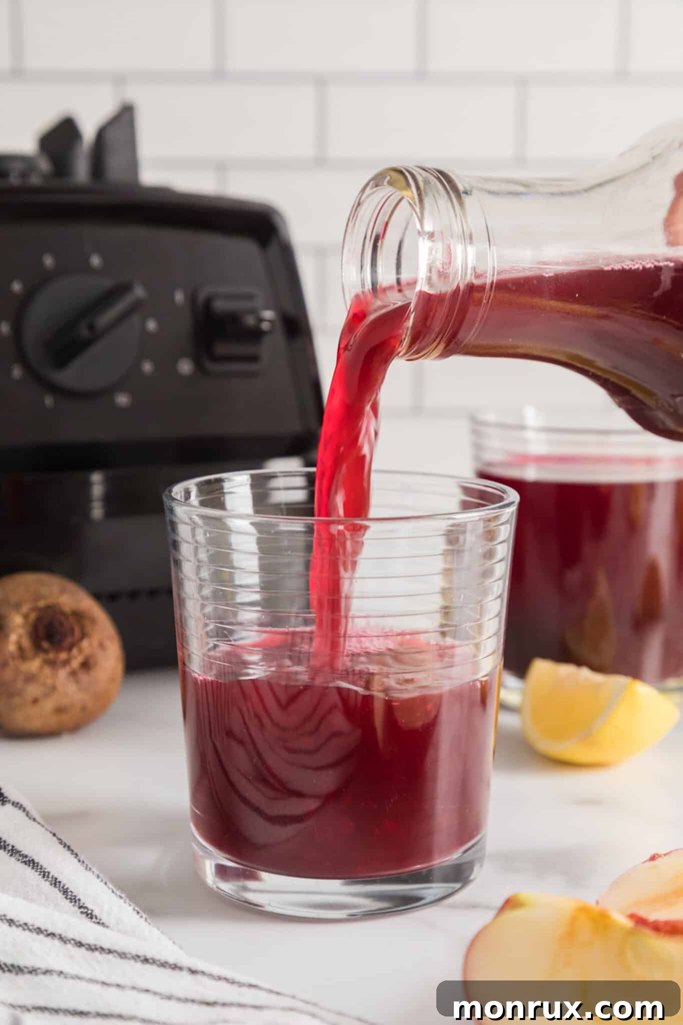 A hand pouring freshly made beet liver cleanse juice into a short glass.