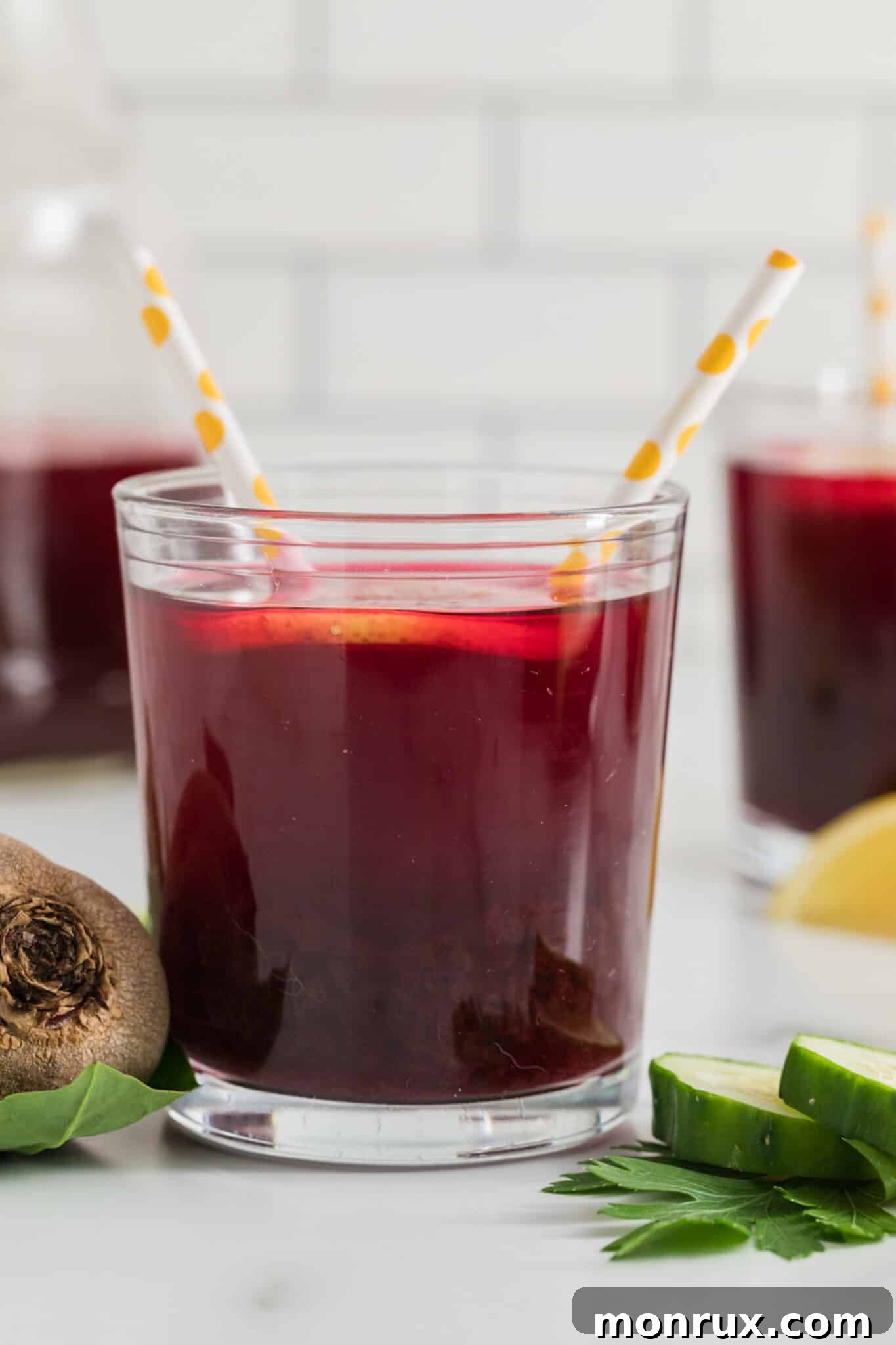 A refreshing glass of beet juice, served with two straws and a lemon slice, highlighting its vibrant color.
