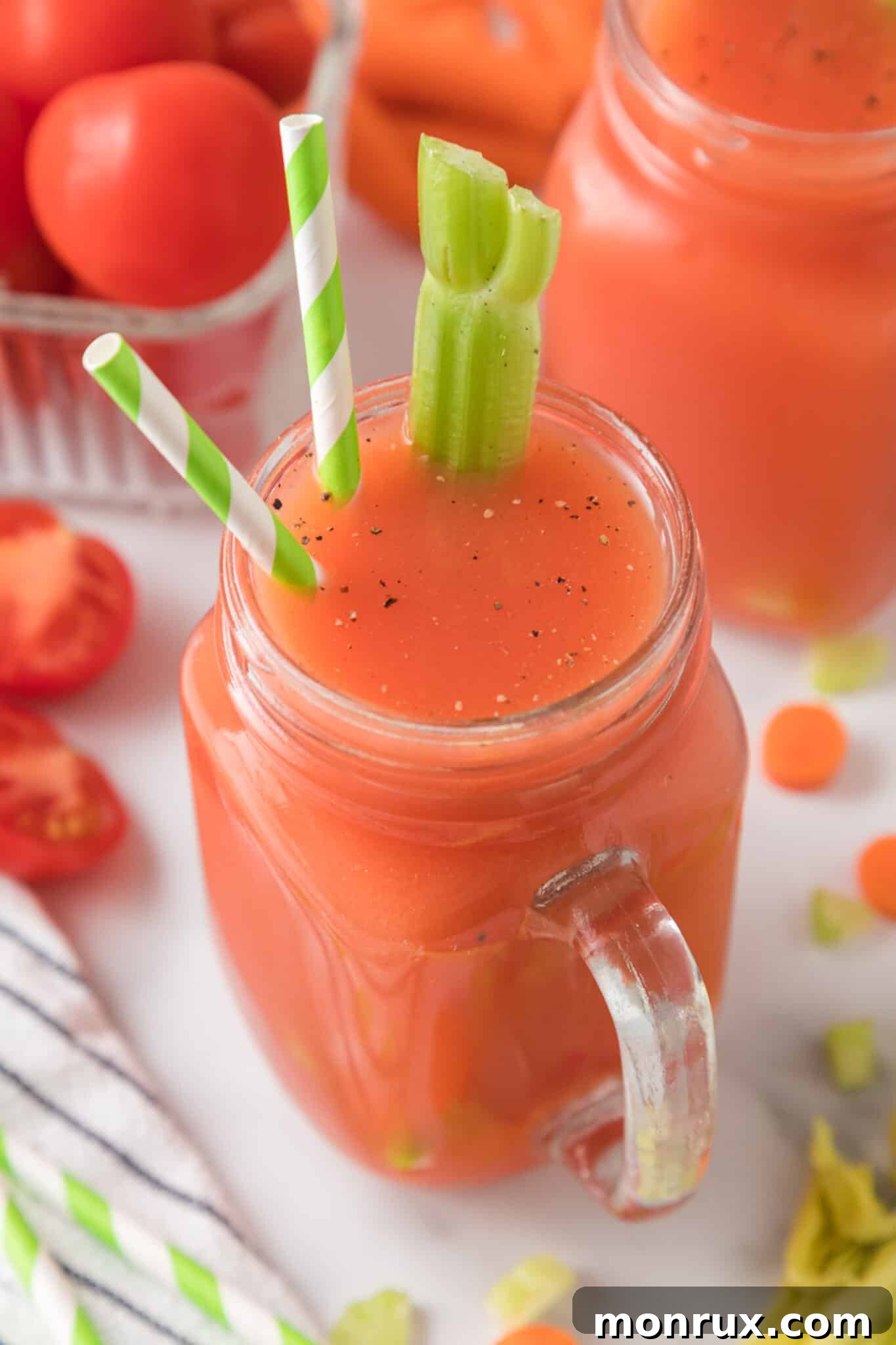 Large handled mason jar with tomato juice that has two straws and a celery stalk.