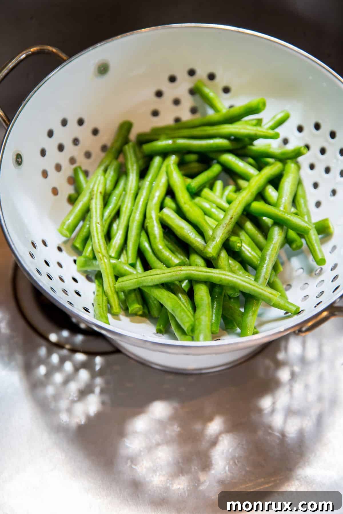 Fresh green beans in a white colander in the sink.