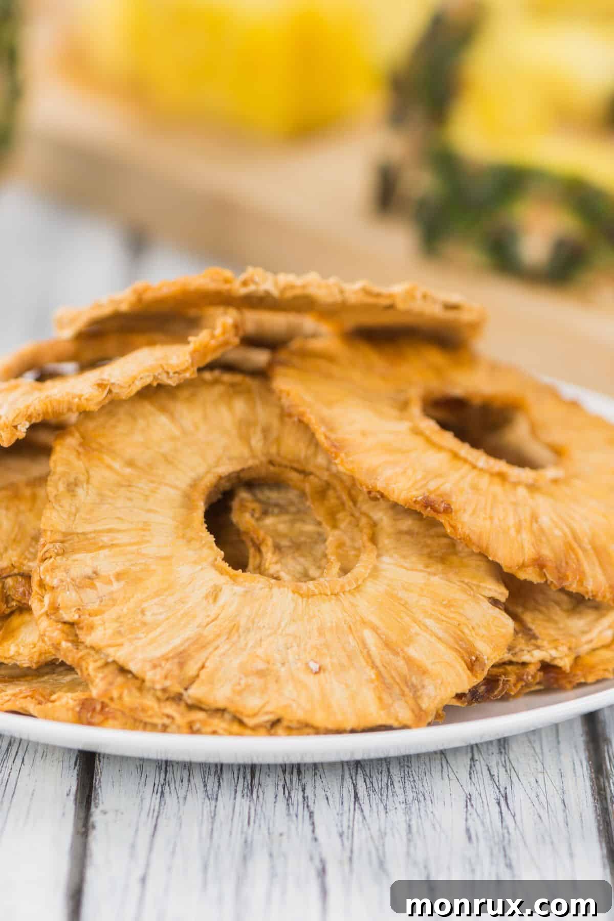 A pile of dehydrated pineapple slices on a white plate, showcasing their golden-brown color and chewy texture.