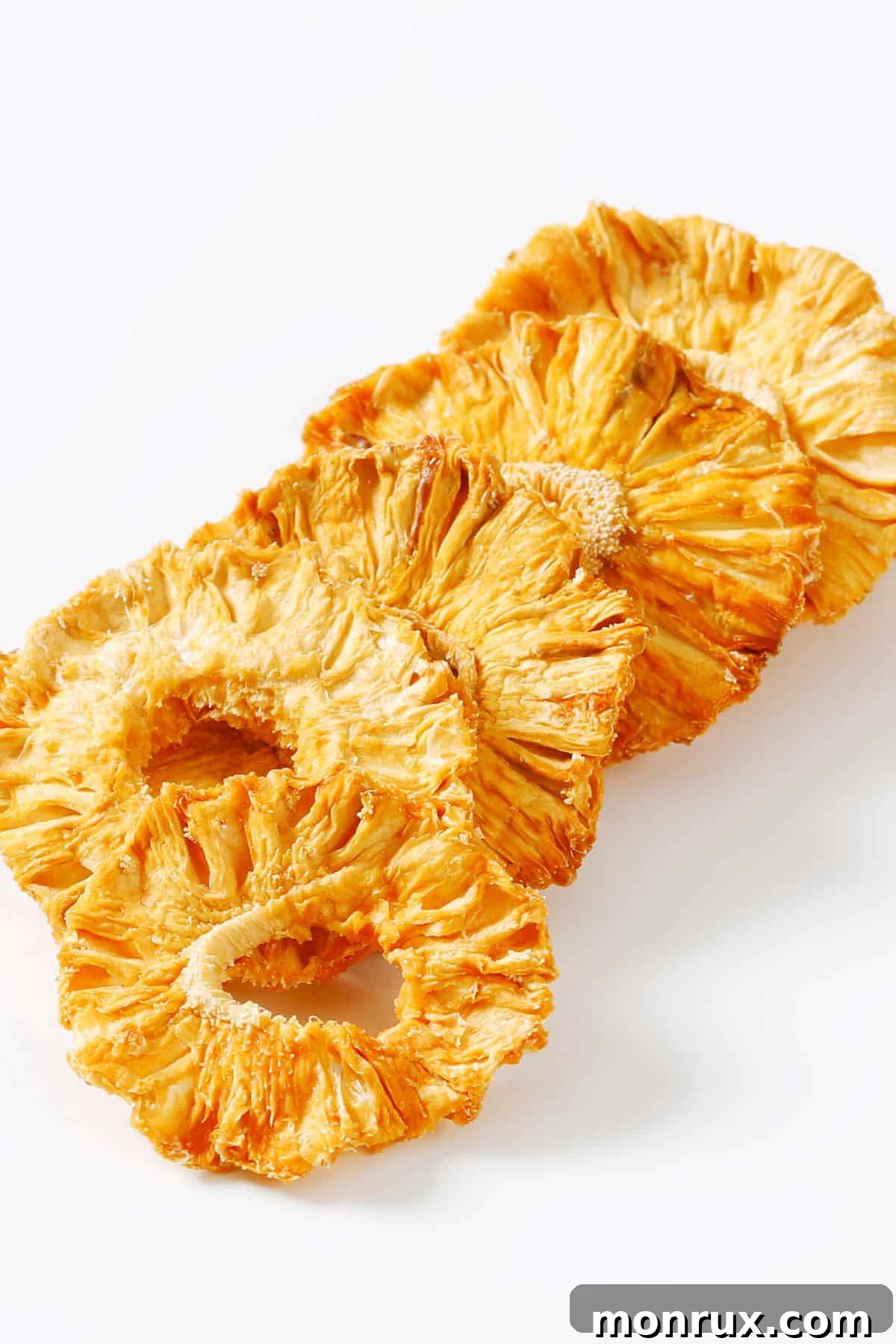 A row of perfectly golden-brown dehydrated pineapple rings laid out on a white surface, ready for storage.