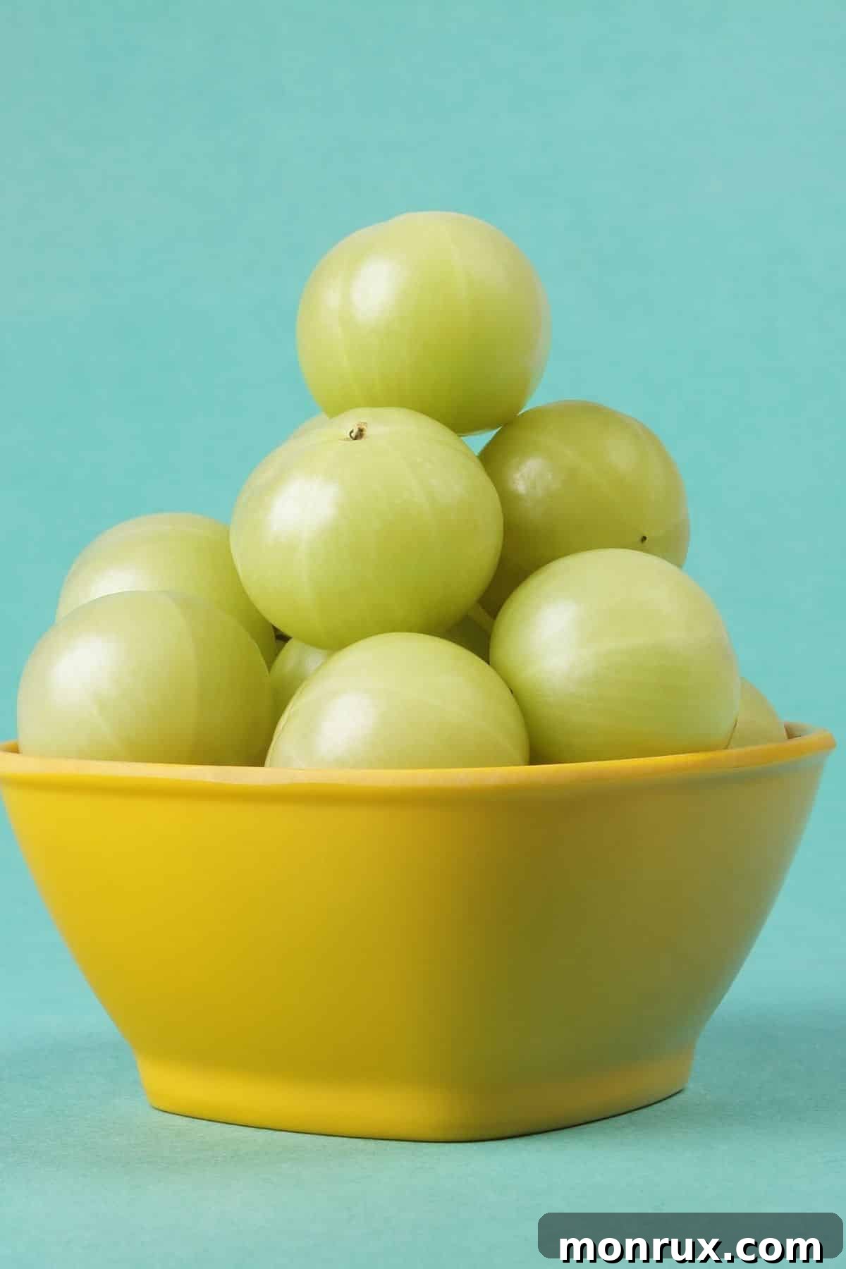 Vibrant yellow bowl generously filled with numerous fresh, green Indian gooseberries, ready for consumption.