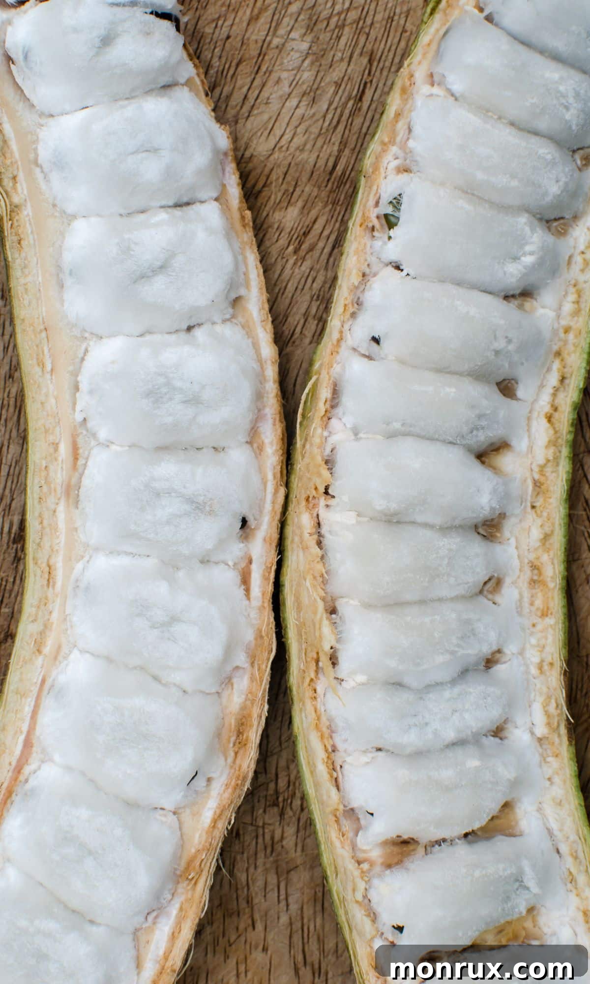 Two long, green ice cream bean pods are split open to reveal their fluffy, white, edible pulp inside.
