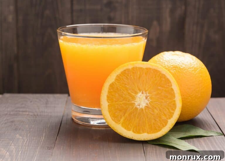 Small glass of orange juice next to two oranges, highlighting fresh ingredients.