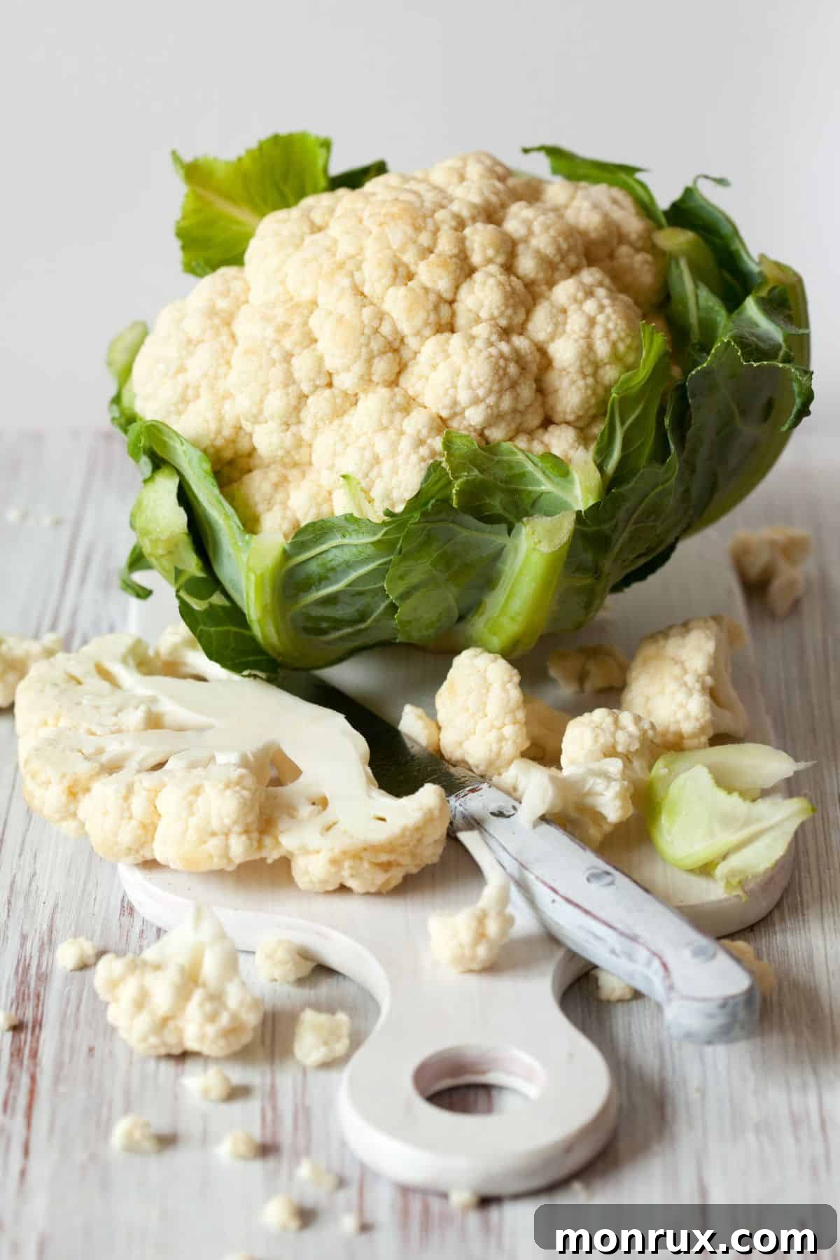 Cauliflower head with cutting board and sliced cauliflower.