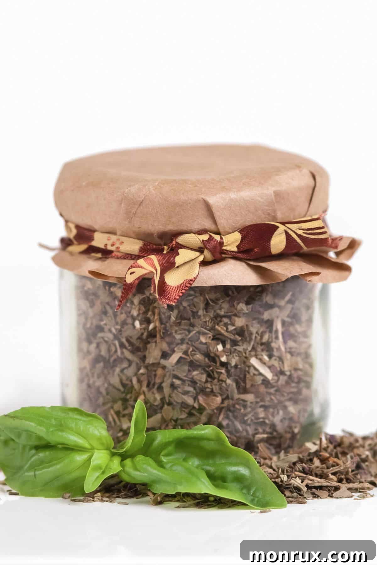 Glass jar filled with dry basil with a paper top.