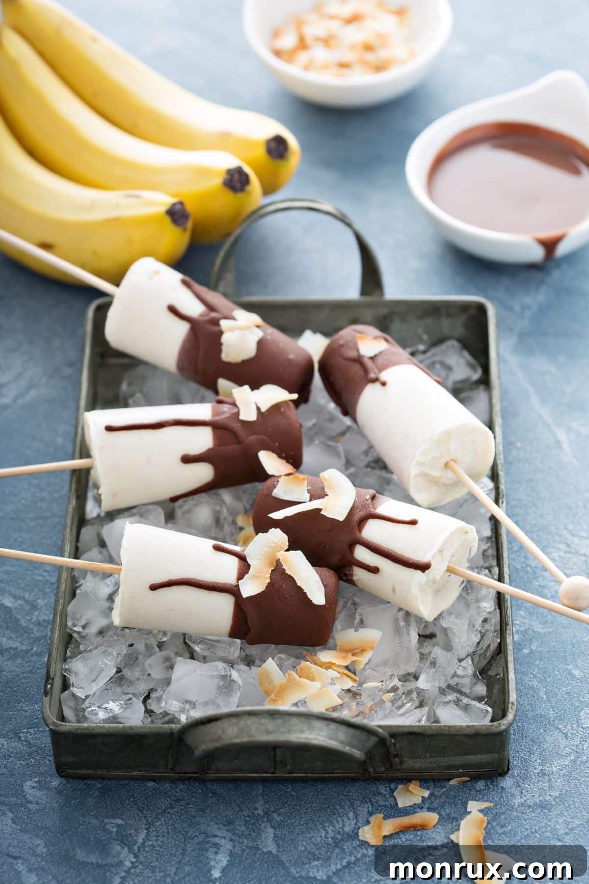 Banana popsicles covered in chocolate sitting in a pan with ice, ready to be enjoyed.