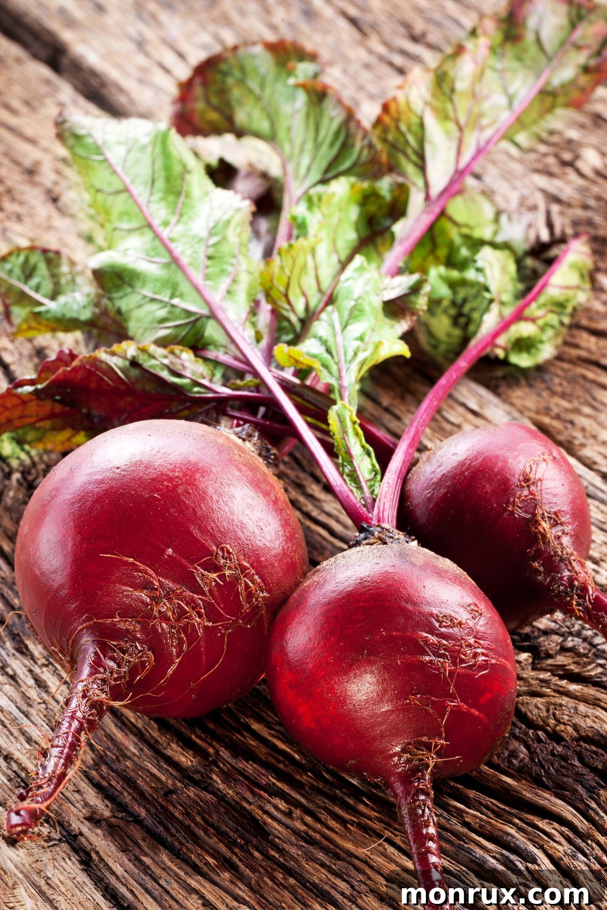 Fresh beets with their greens still attached, laid on a rustic wooden table.