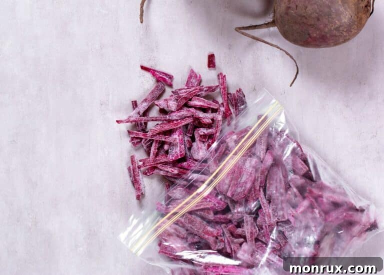 A baggie of frozen shredded beets next to two whole beets, ready for freezing.