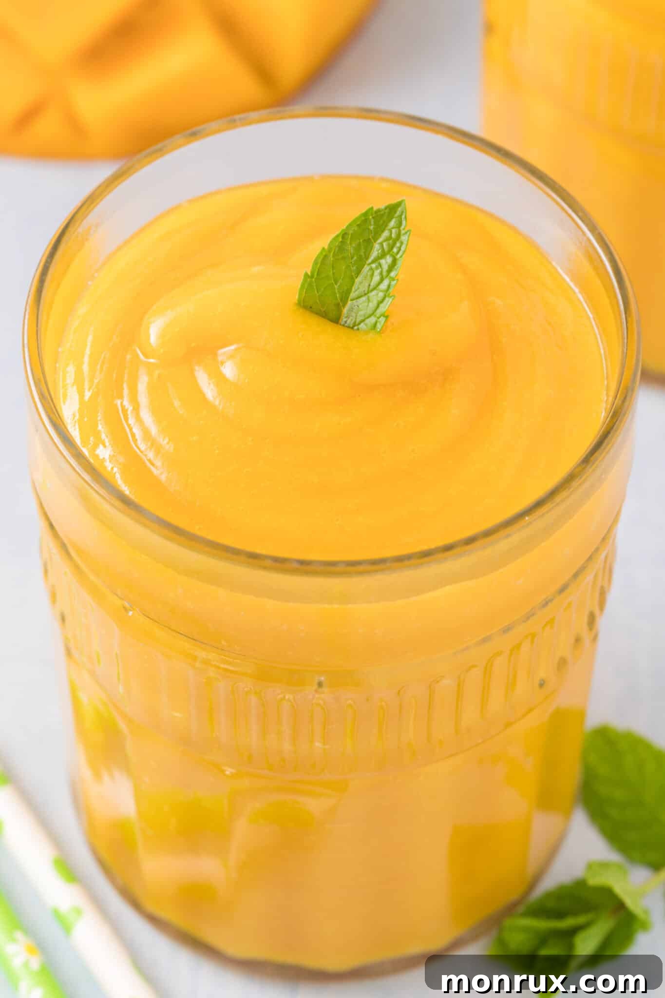A refreshing glass of homemade mango juice, garnished with a fresh mint leaf, set against a bright, sunny background.