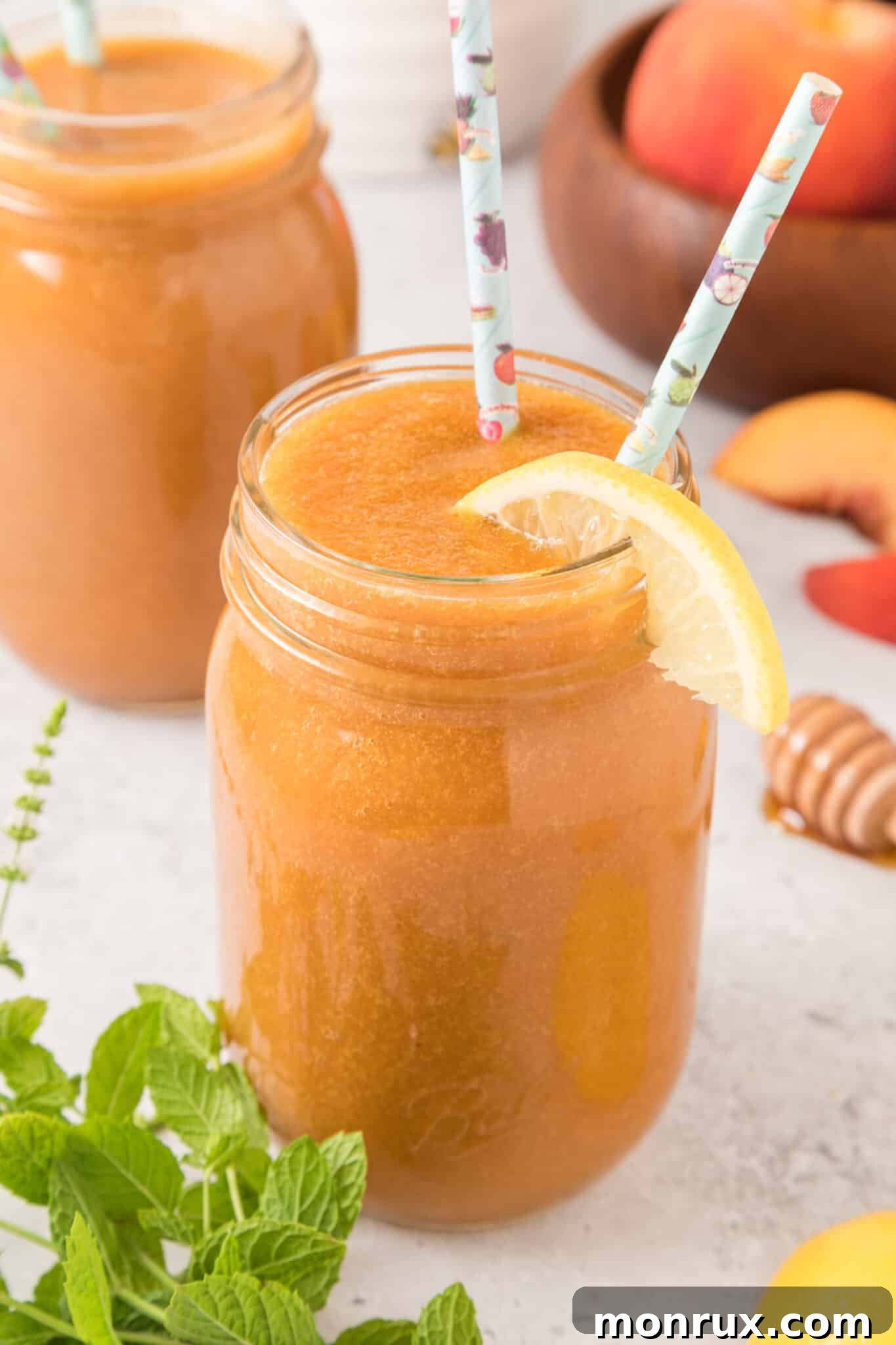 A glass pitcher and a jar of freshly made peach juice, garnished with lemon and peach slices, sitting on a wooden surface.