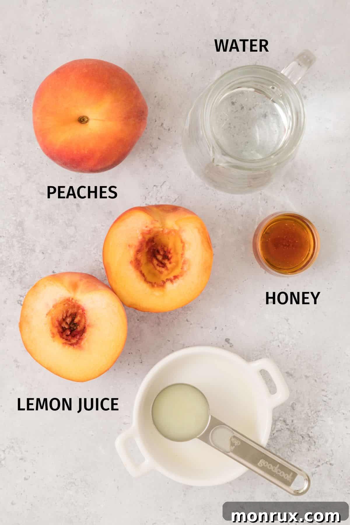Fresh peaches, a lemon, and a jar of honey on a white surface, ready to be made into juice.