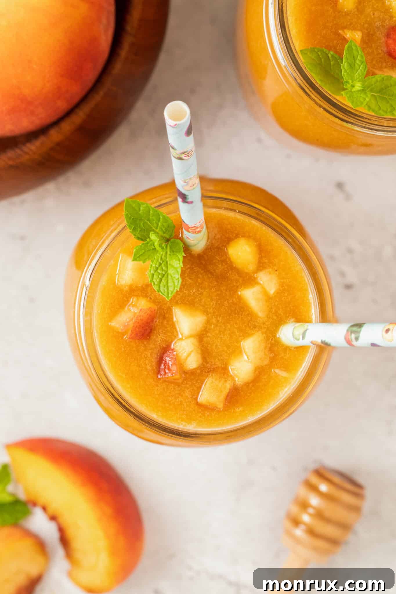 Two Mason jars filled with peach juice, garnished with peach chunks and mint, with two straws.